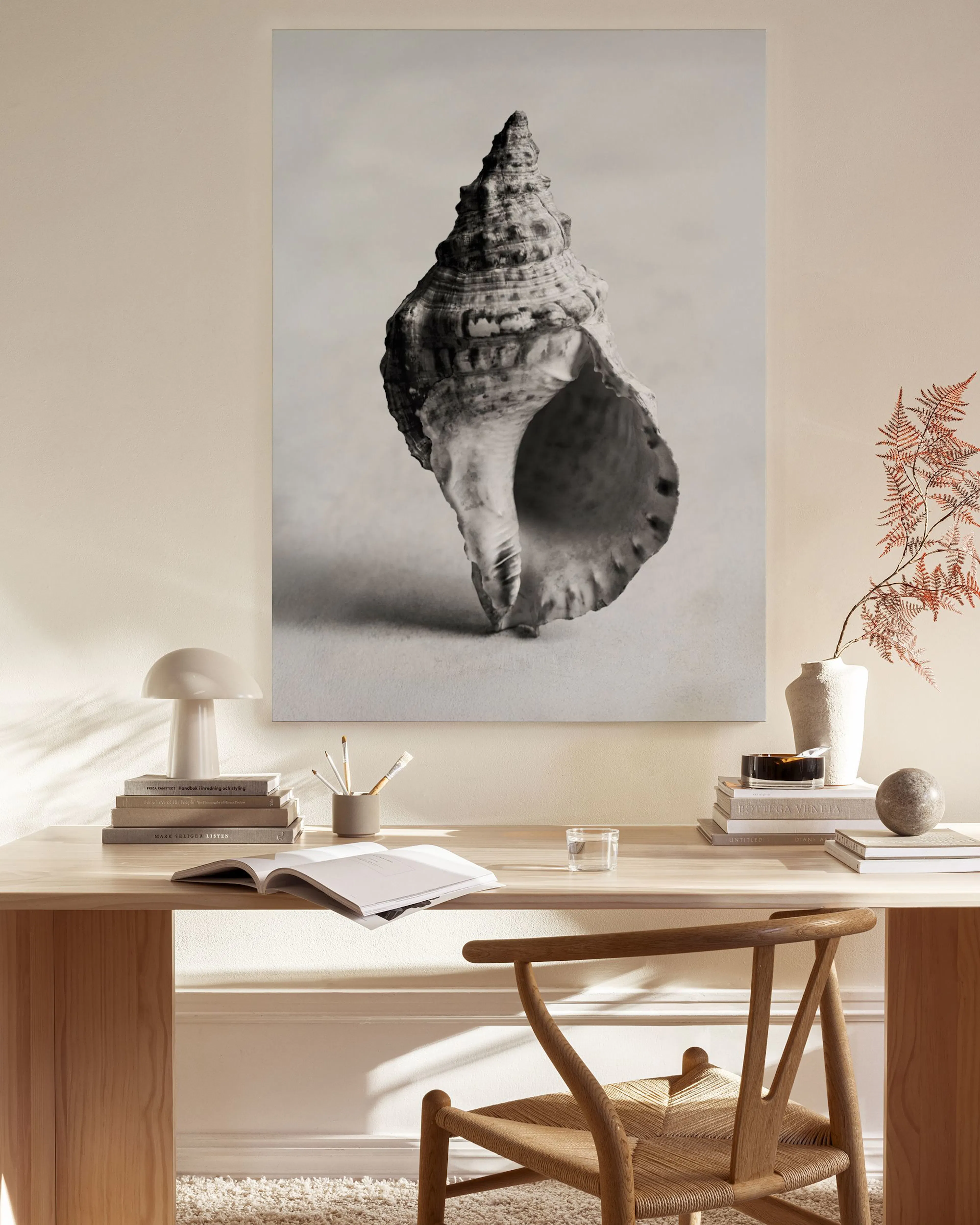 A black and white canvas print of a spiral seashell in a light-toned living room with a wooden chair and coffee table.