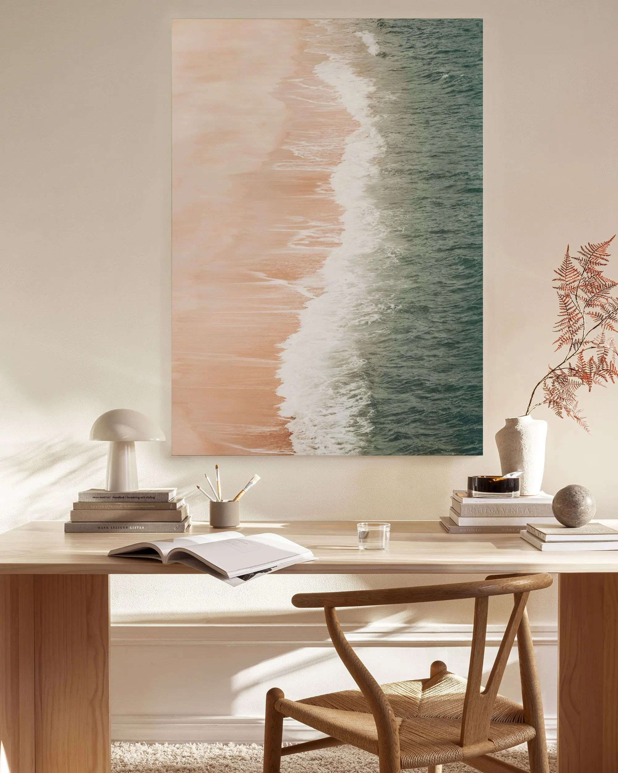 Toile murale dune plage vue du dessus avec sable rose et vagues vertes, accrochée dans un salon lumineux.