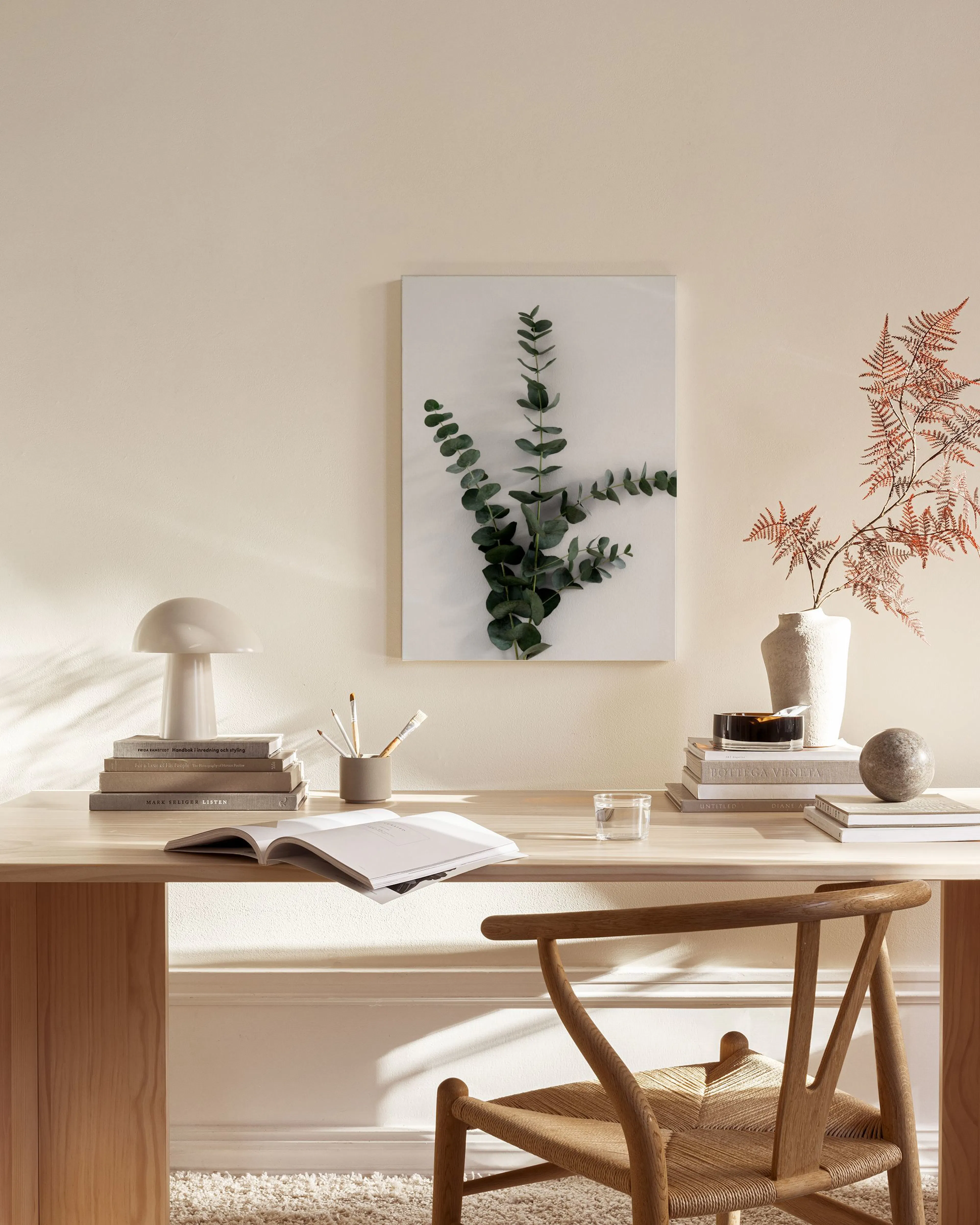 A canvas print of eucalyptus branches on a white background, hanging in a bright, minimalist living room above a wooden console.