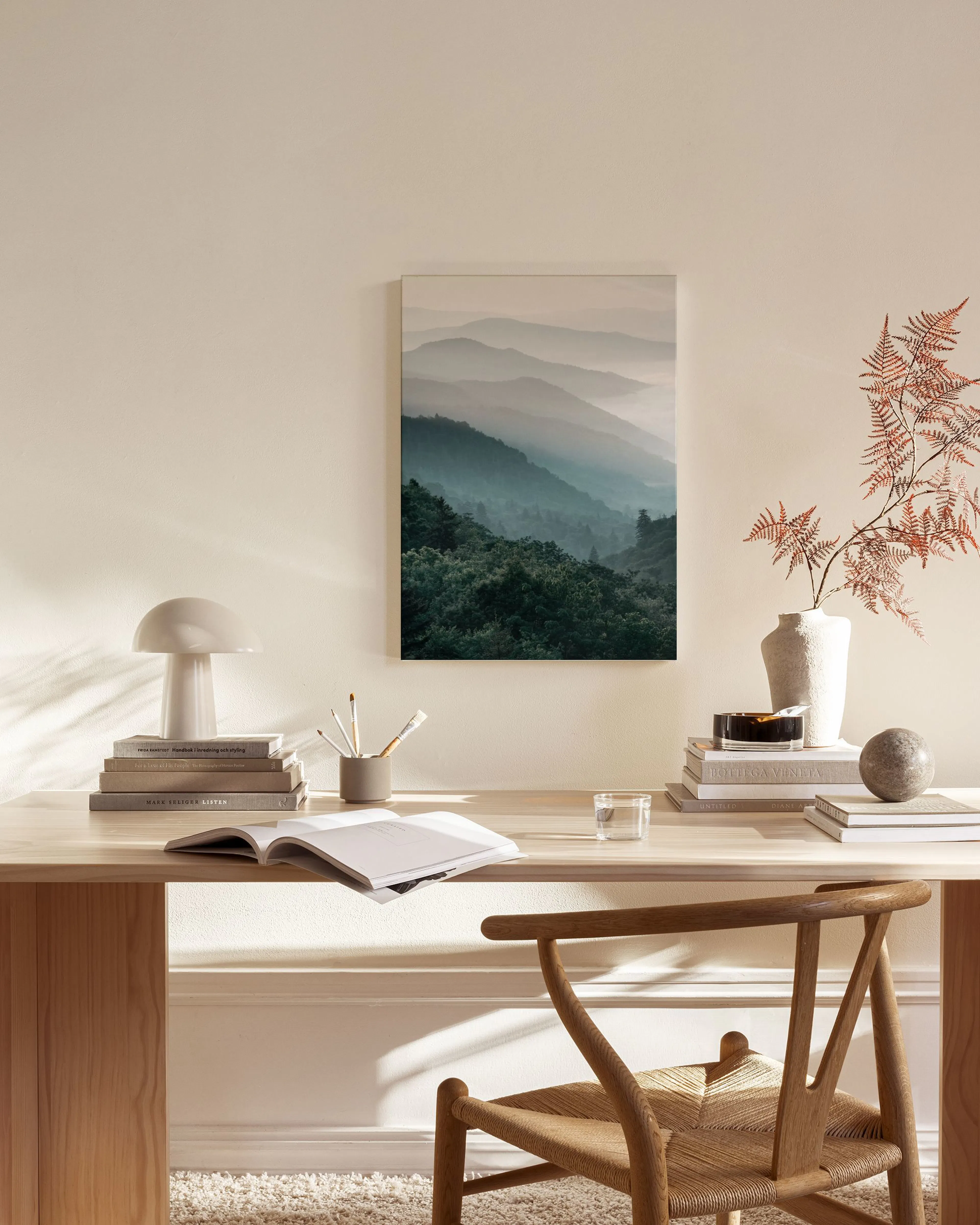 Tela decorativa de paisagem montanhosa com neblina, tons de azul e verde, pendurada numa sala de estar moderna.