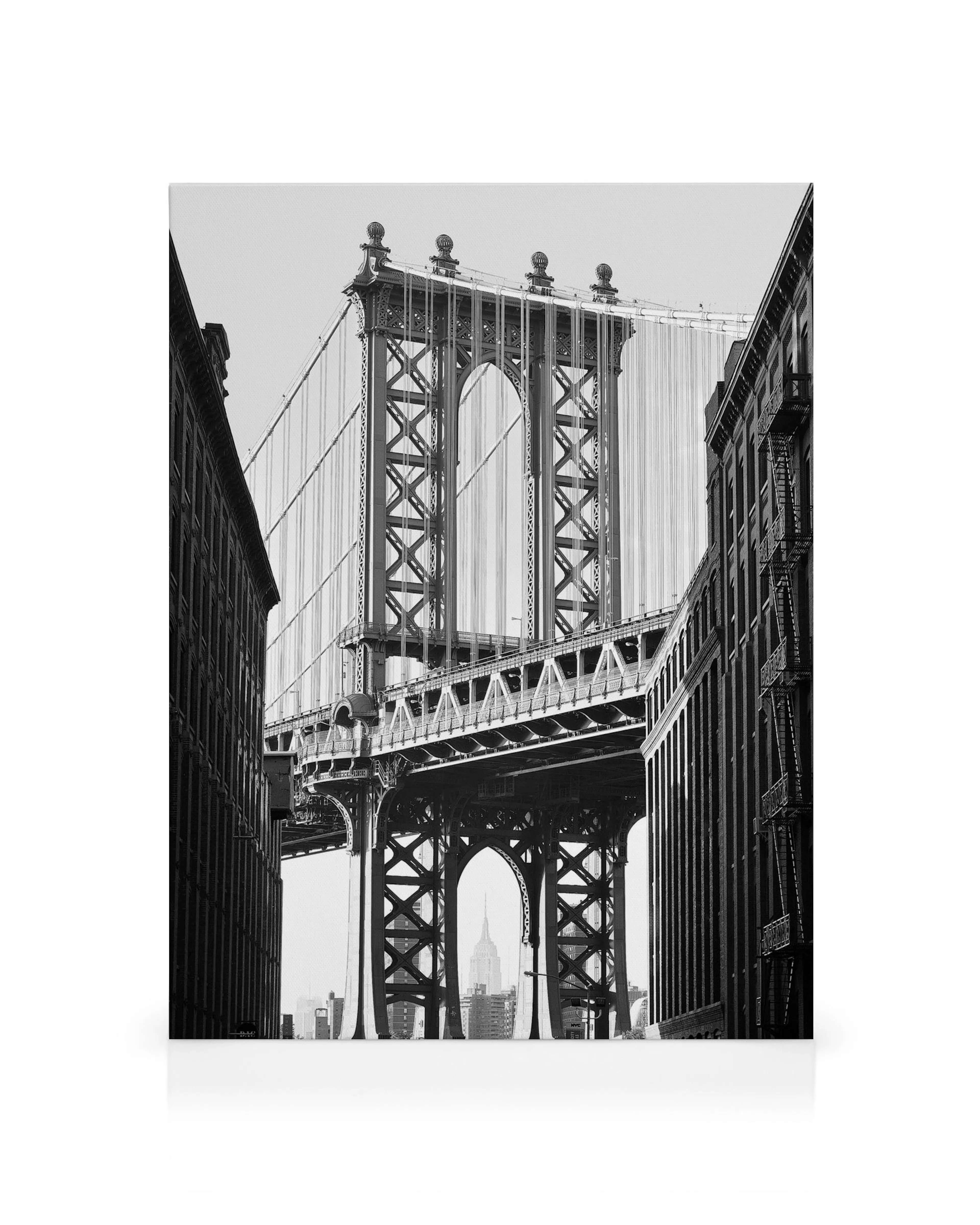 Sort/hvid Manhattan Bridge i New York, set nedefra med bygningerne på hver side. Empire State Building ses i baggrunden.