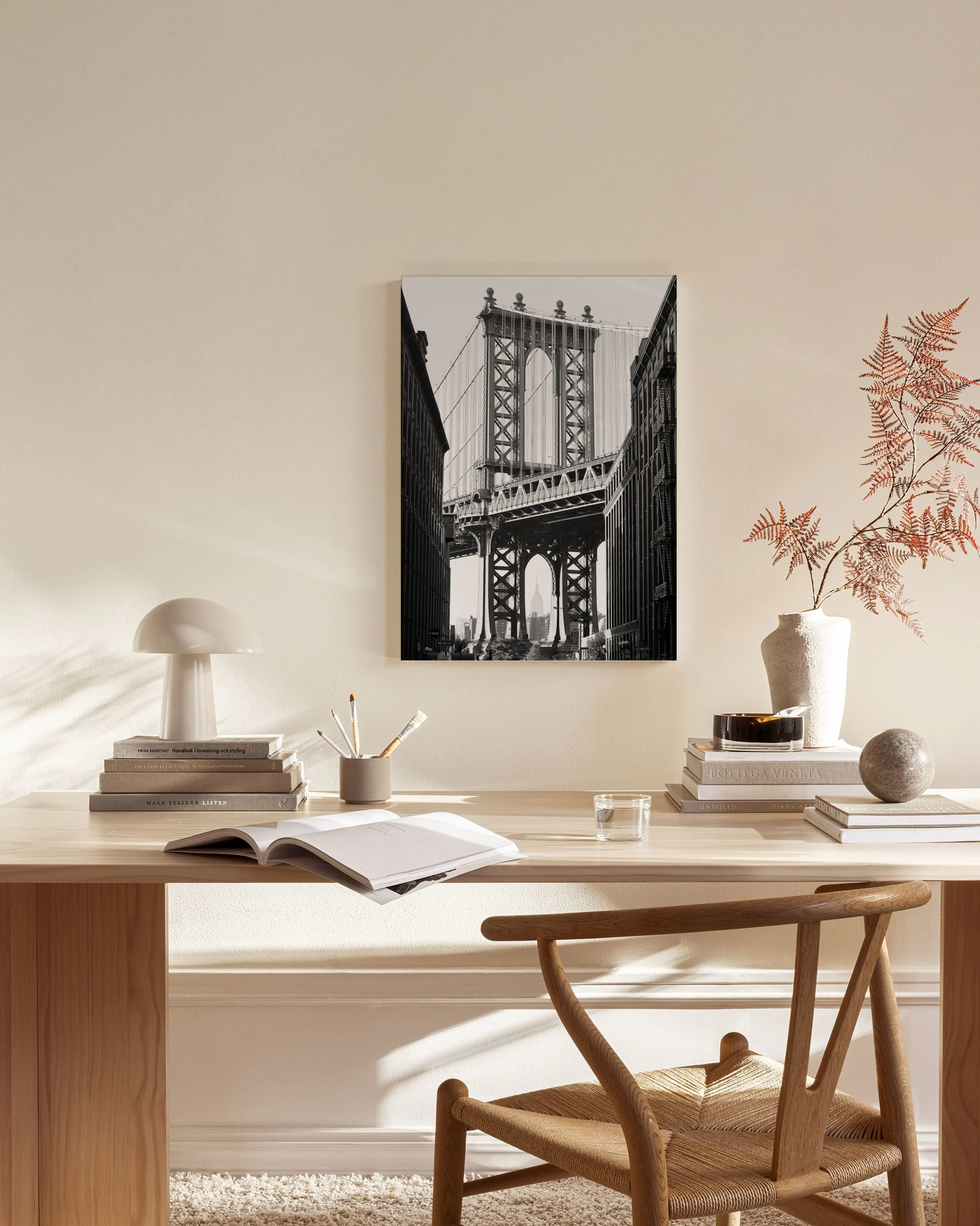 Černobílý obraz na plátně s Manhattanským mostem v New Yorku, visící v moderním obývacím pokoji s dřevěným nábytkem.