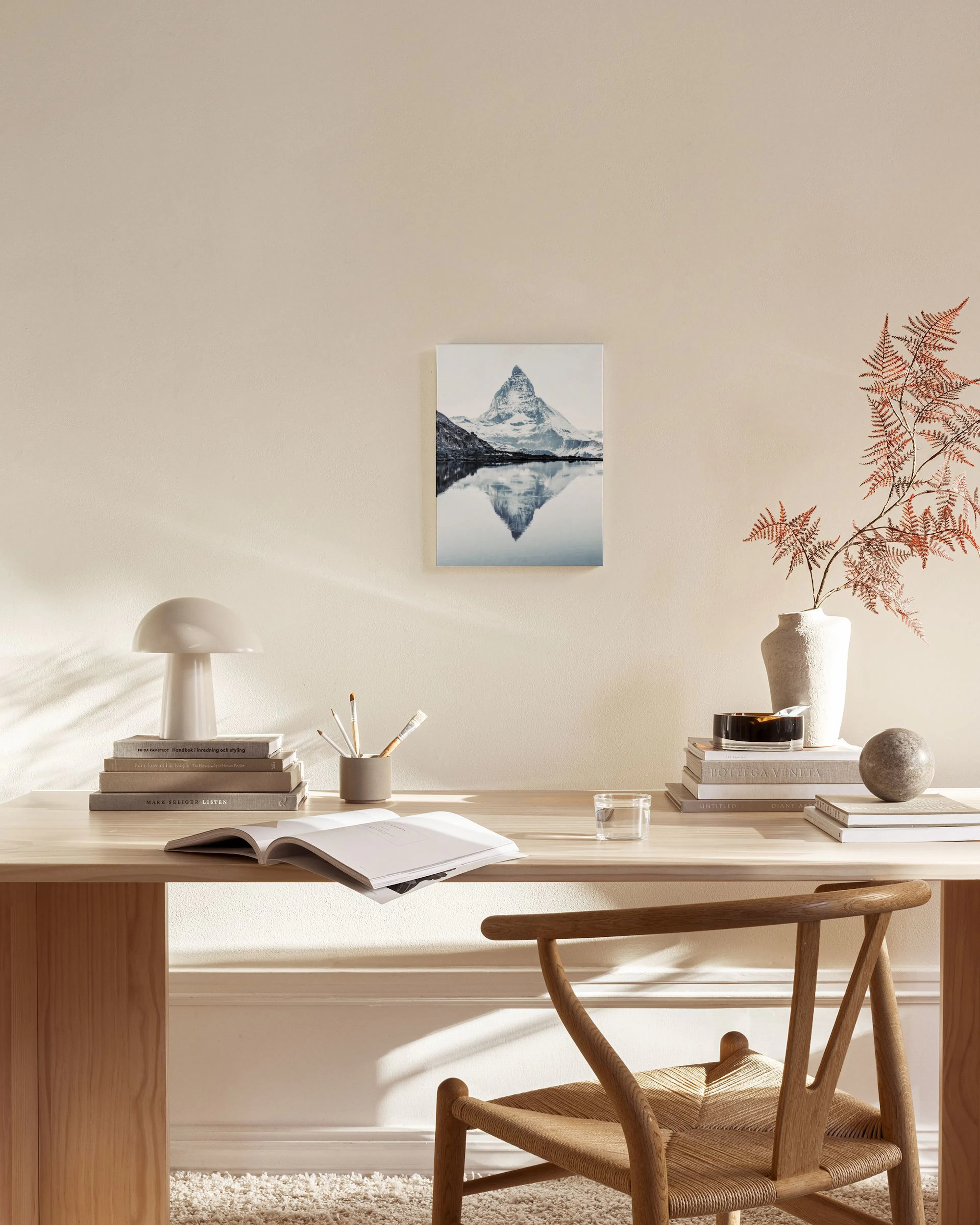 A monochromatic mountain peak reflected in a calm lake, hanging in a bright, modern living room with light wood furniture.