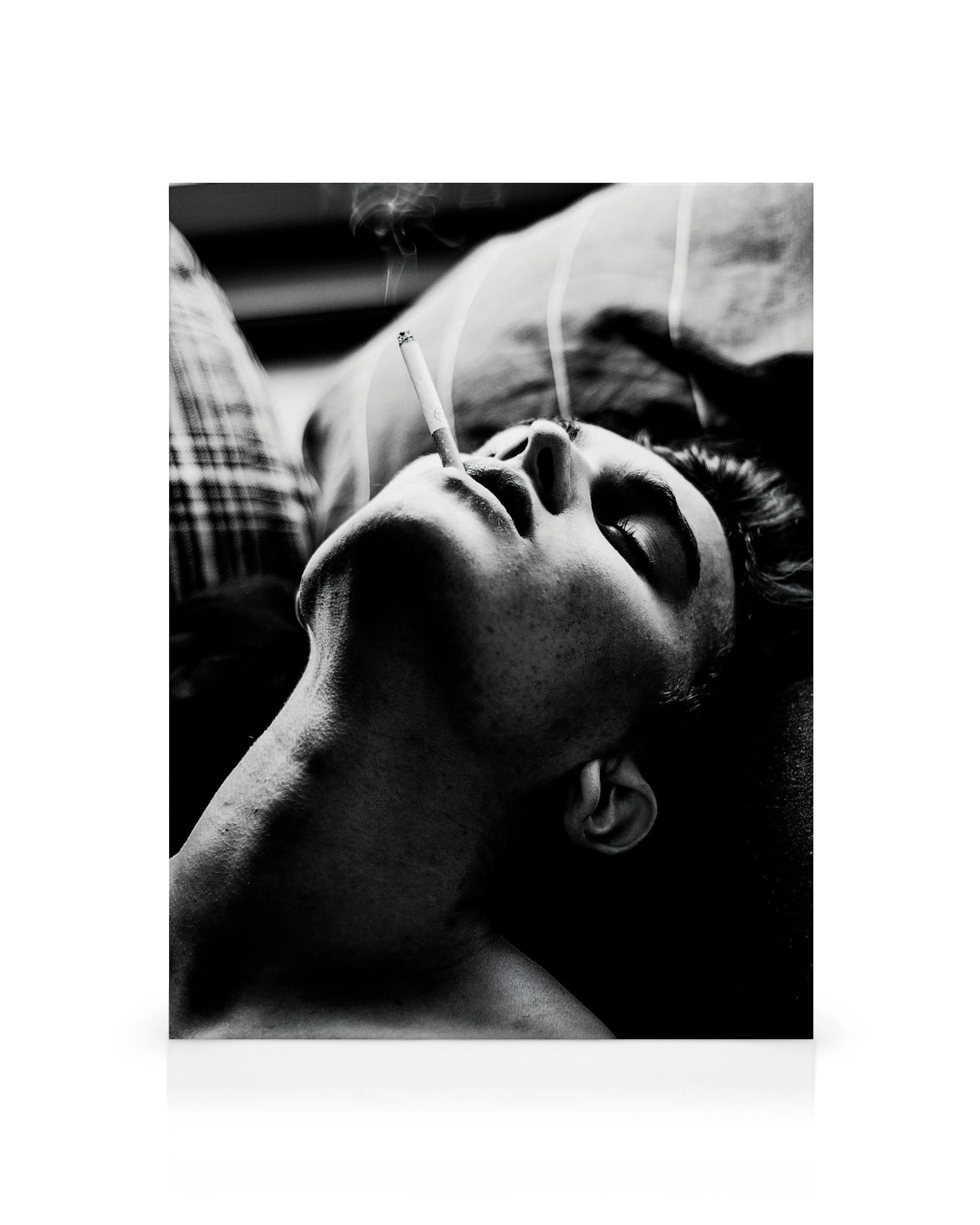 Čiernobiely portrét muža s cigaretou v ústach, dym stúpa, leží na chrbte. Smoking in Bed obraz.