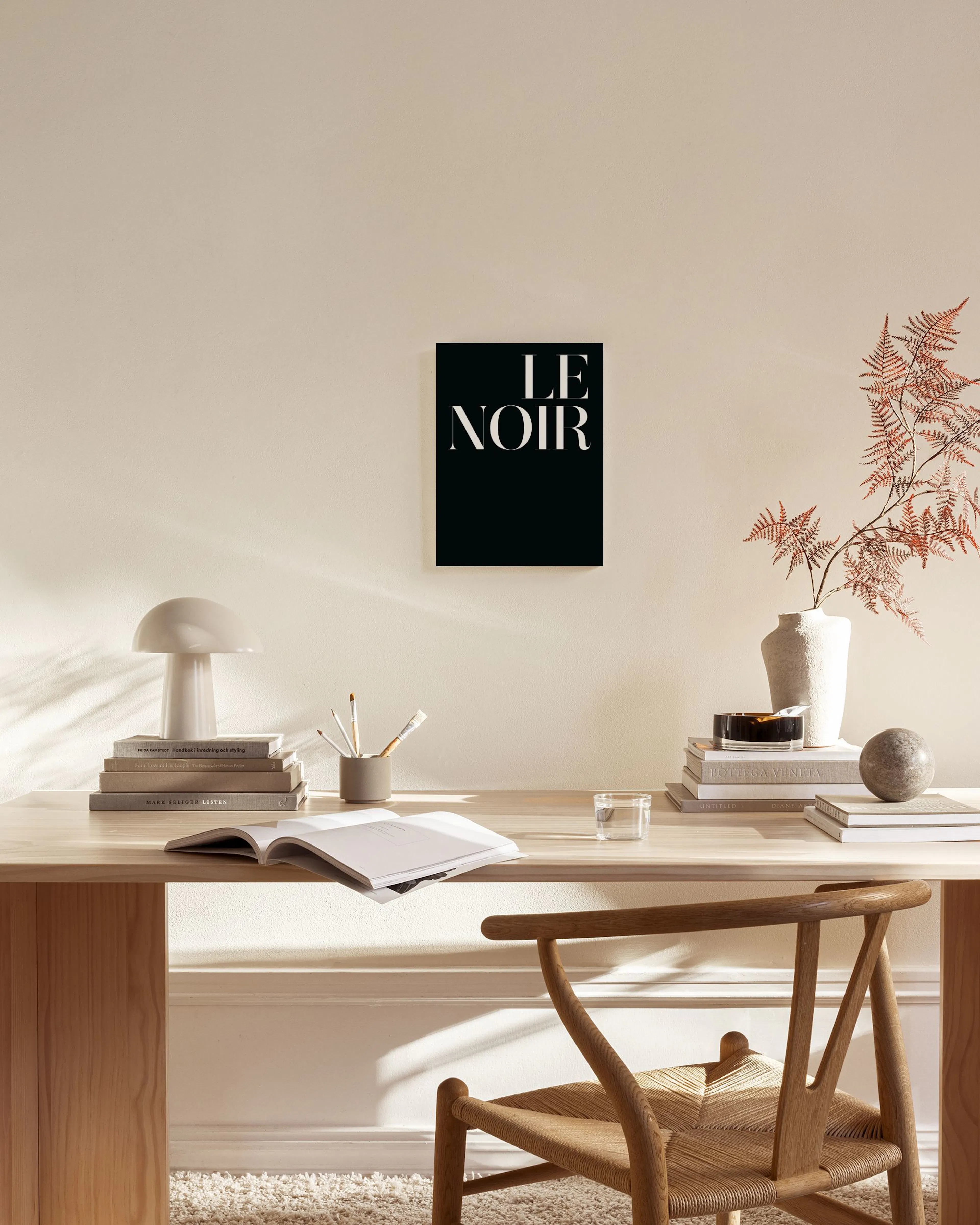 Toile noire avec le texte LE NOIR en blanc, accrochée au mur clair dun salon moderne avec une chaise en bois et une table basse.
