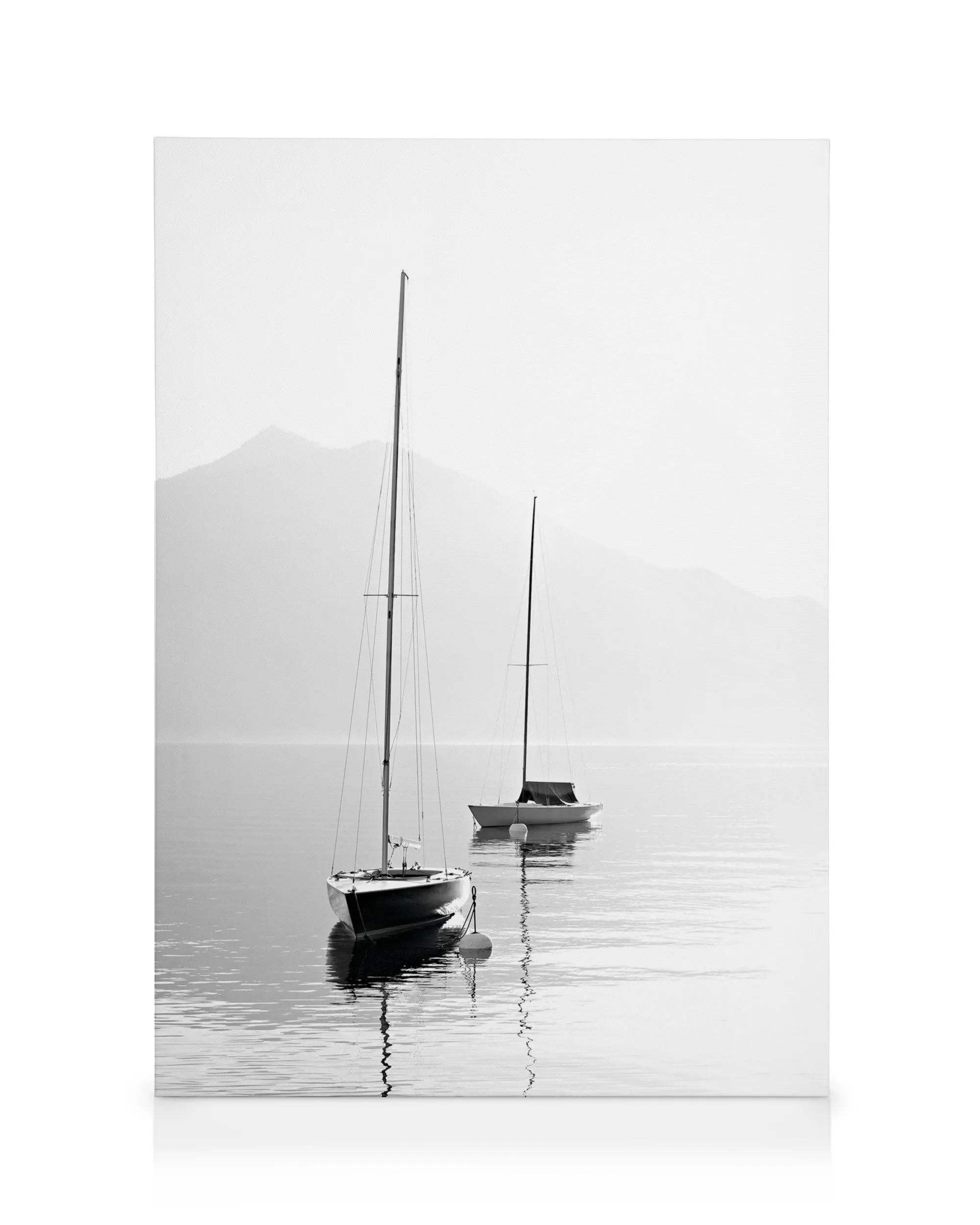 Toile noir et blanc de deux voiliers sur leau calme avec des montagnes floues à larrière-plan.