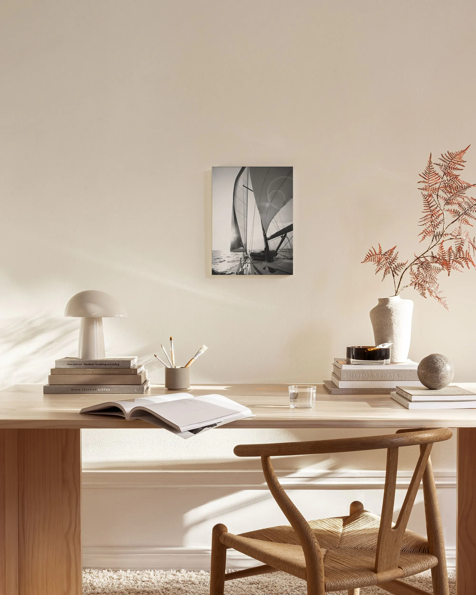 Tela decorativa de um veleiro em preto e branco, com o sol a brilhar nas velas, pendurada num ambiente de sala de estar moderna.