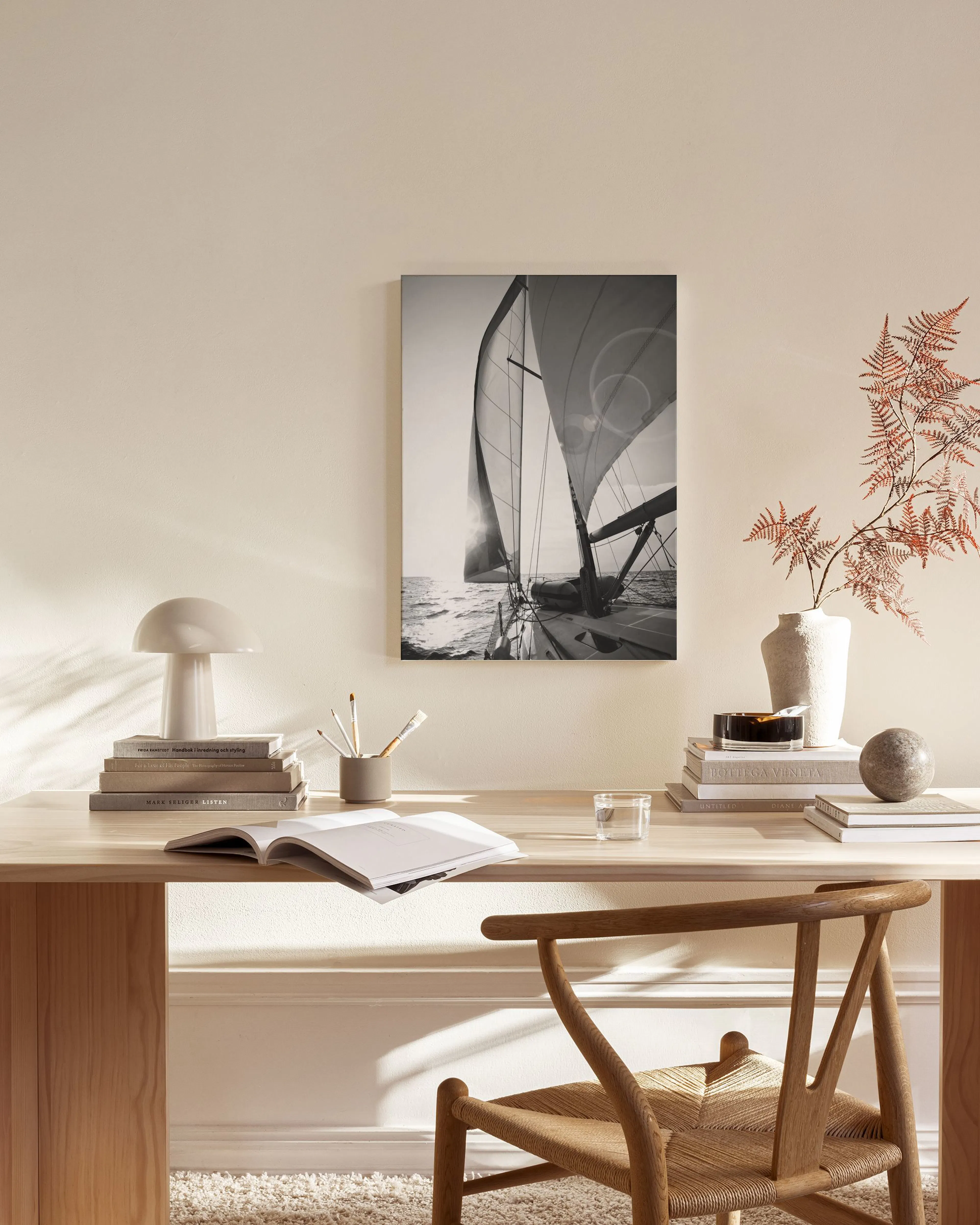 A monochrome canvas print of a sailboat on the ocean with sun glare, displayed in a modern living room.