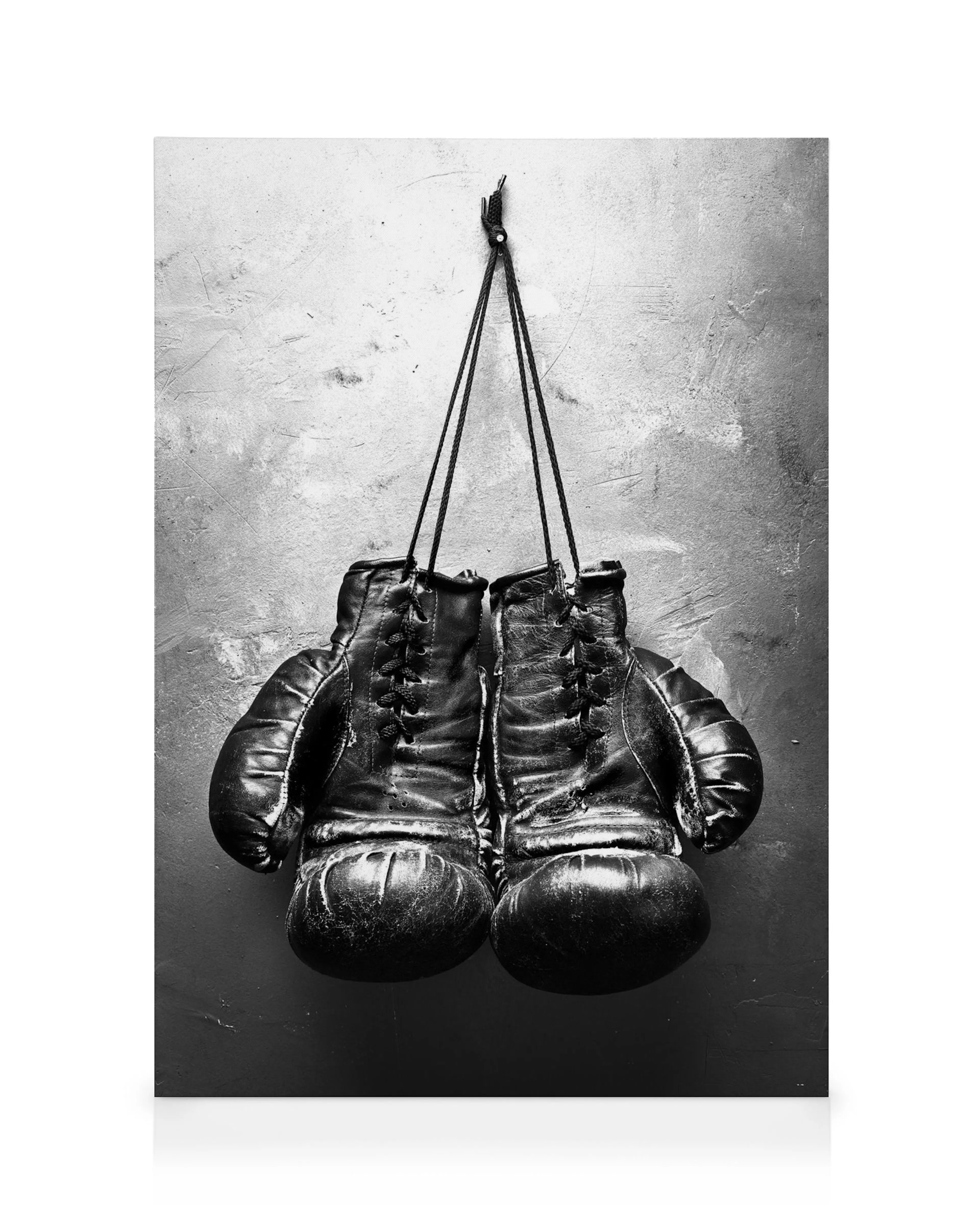 Tela com luvas de boxe pretas penduradas em prego, fundo cinza texturizado, estilo monocromático.
