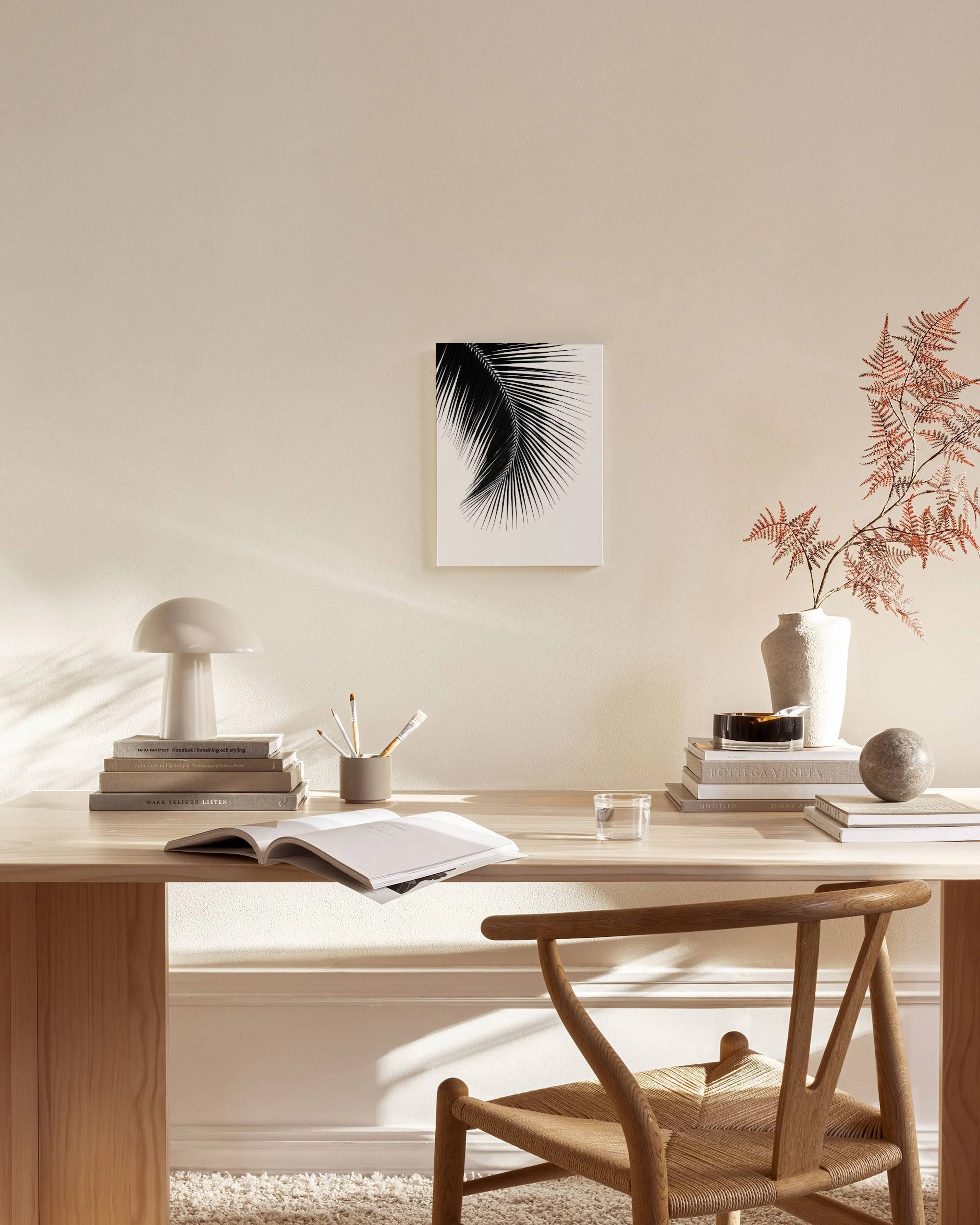Toile murale en noir et blanc dune feuille de palmier, suspendue dans un salon beige au-dessus dun meuble en bois.