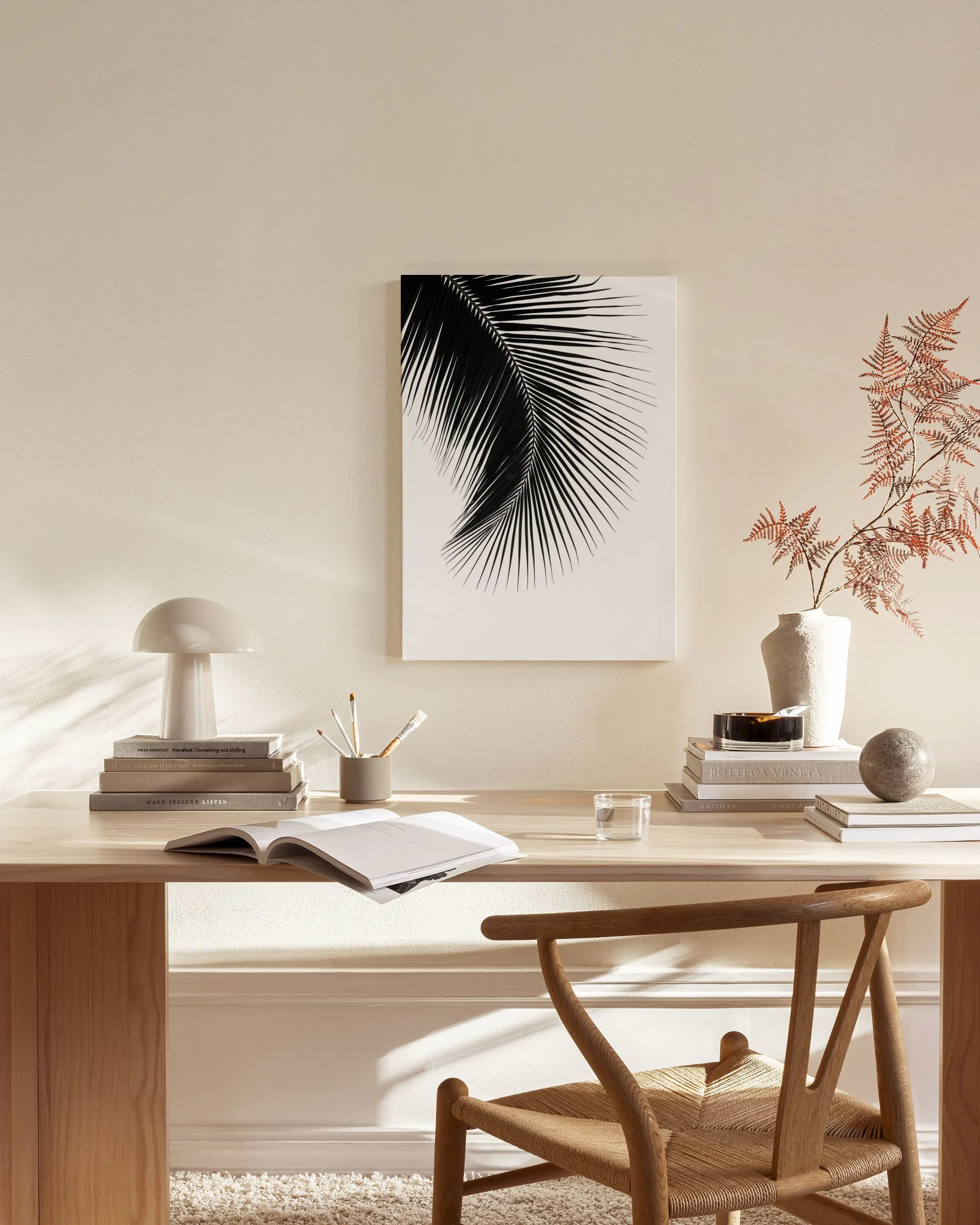Toile murale en noir et blanc dune feuille de palmier, suspendue dans un salon beige au-dessus dun meuble en bois.