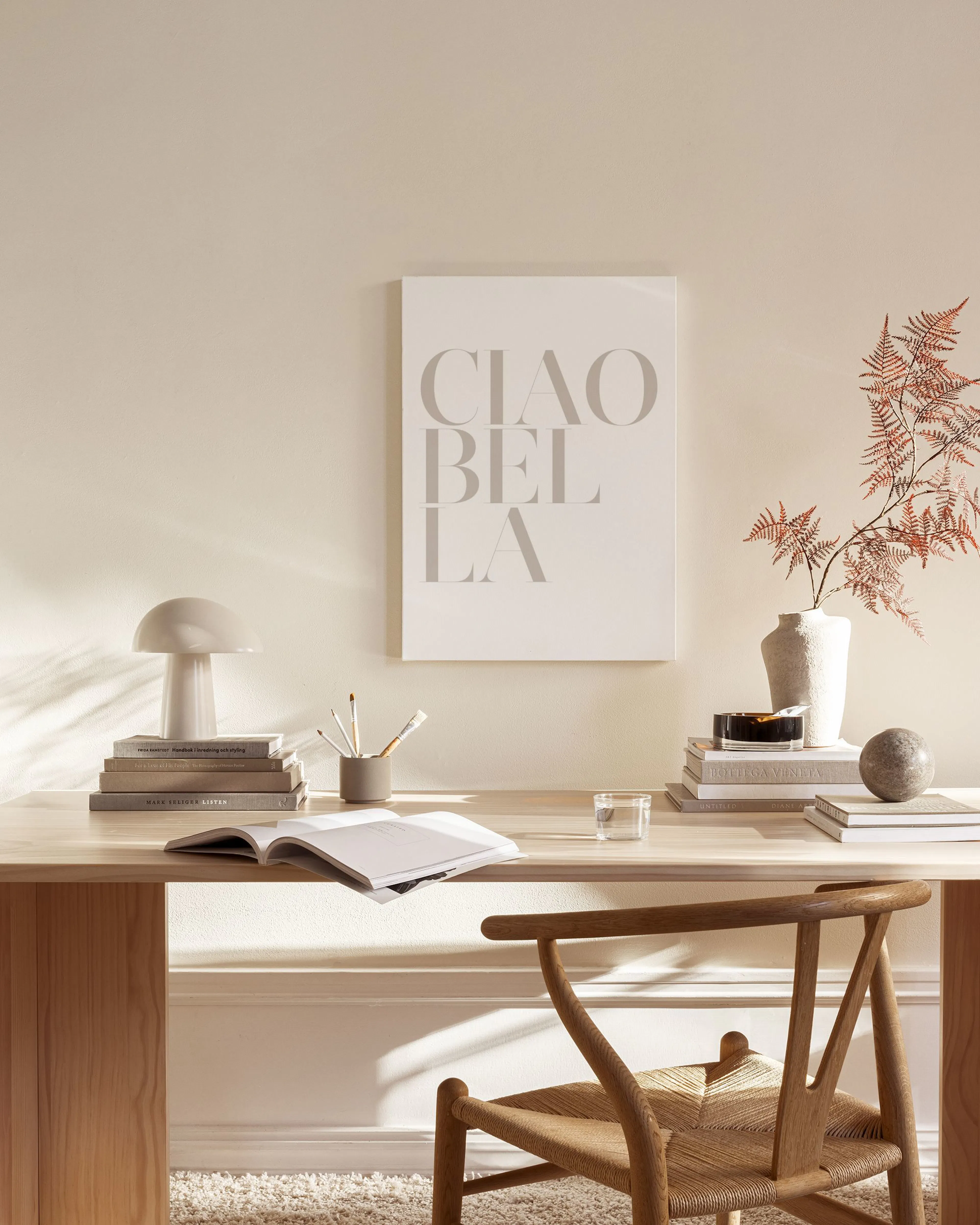 Canvas met CIAO BELLA in beige letters, hangend in een neutrale woonkamer boven een houten dressoir.