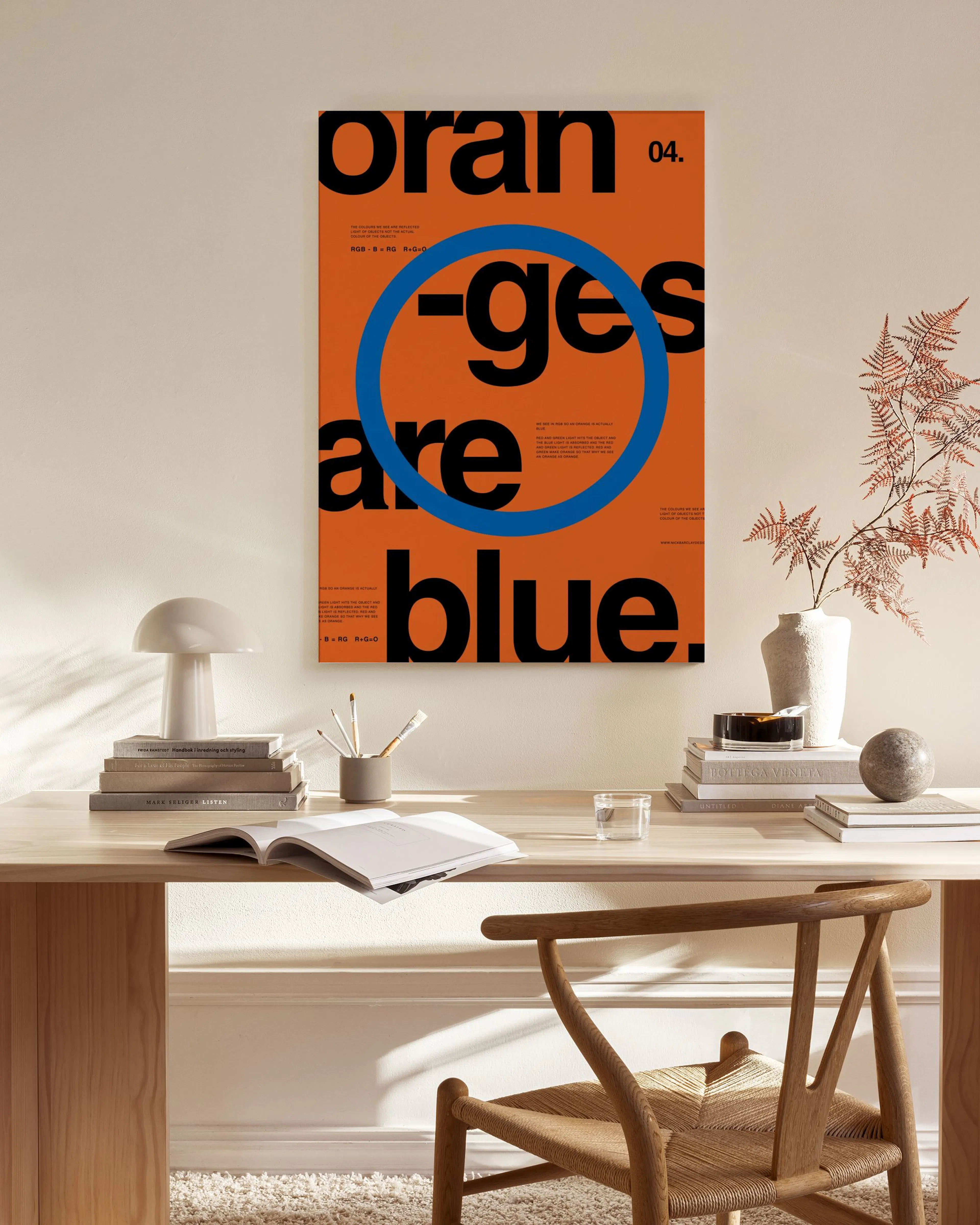 A canvas print with Oranges are blue in black text and a blue circle on an orange background, hanging in a minimalist living roo