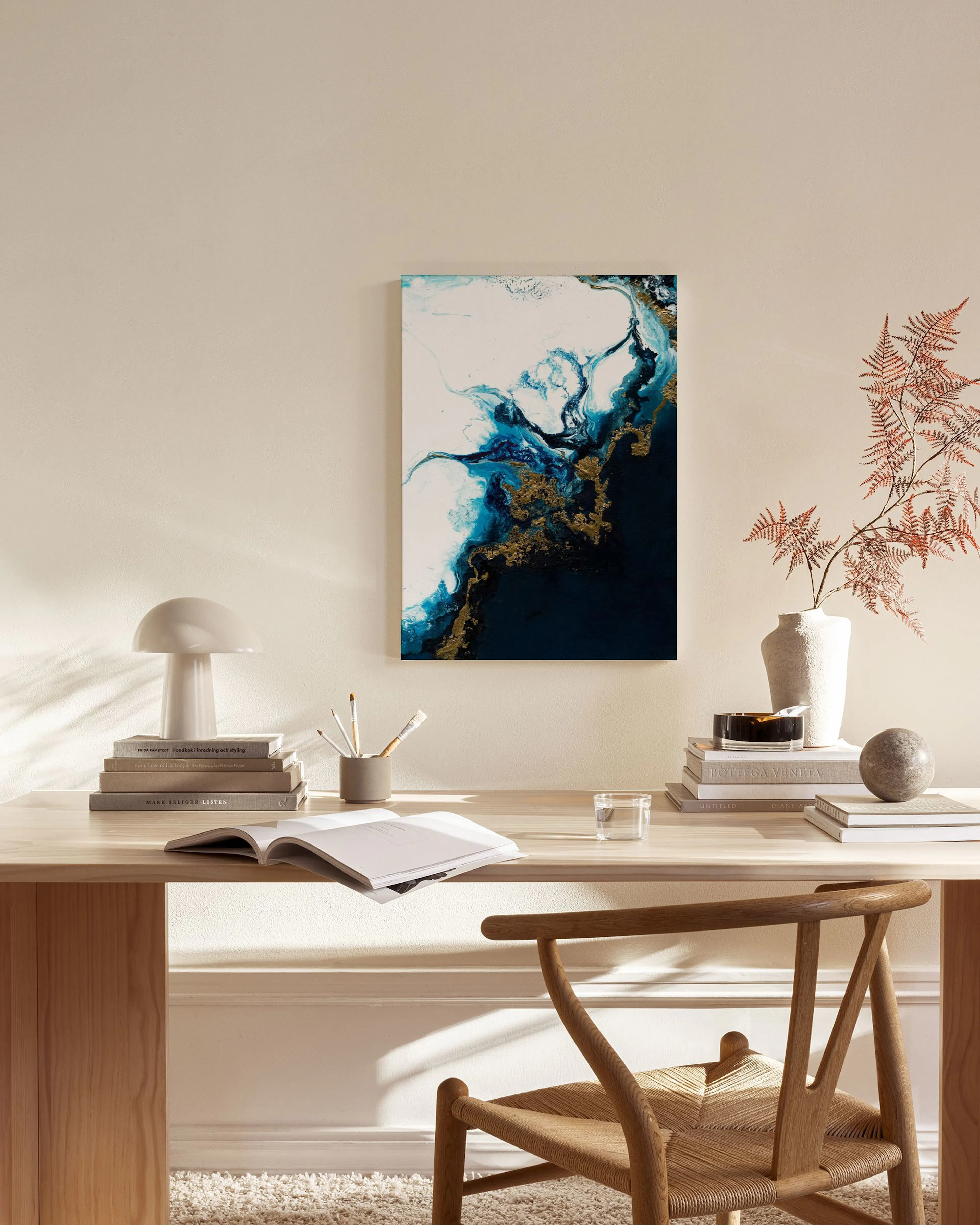 Toile abstraite bleu marine, blanche et dorée, accrochée au mur dun salon moderne avec fauteuil en bois et table basse.