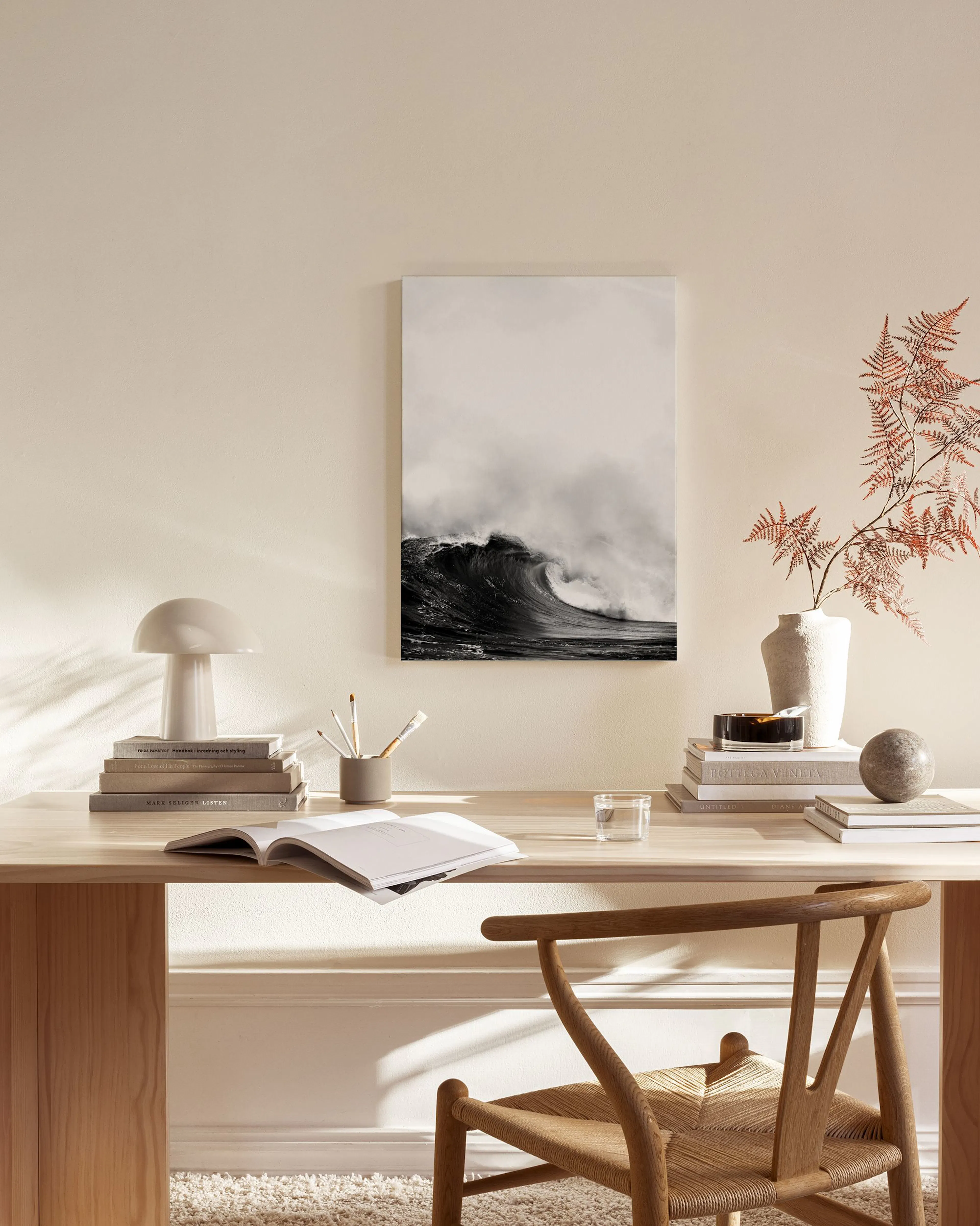 Toile de vague océanique en noir et blanc, suspendue dans un salon moderne avec fauteuil en bois et table basse.