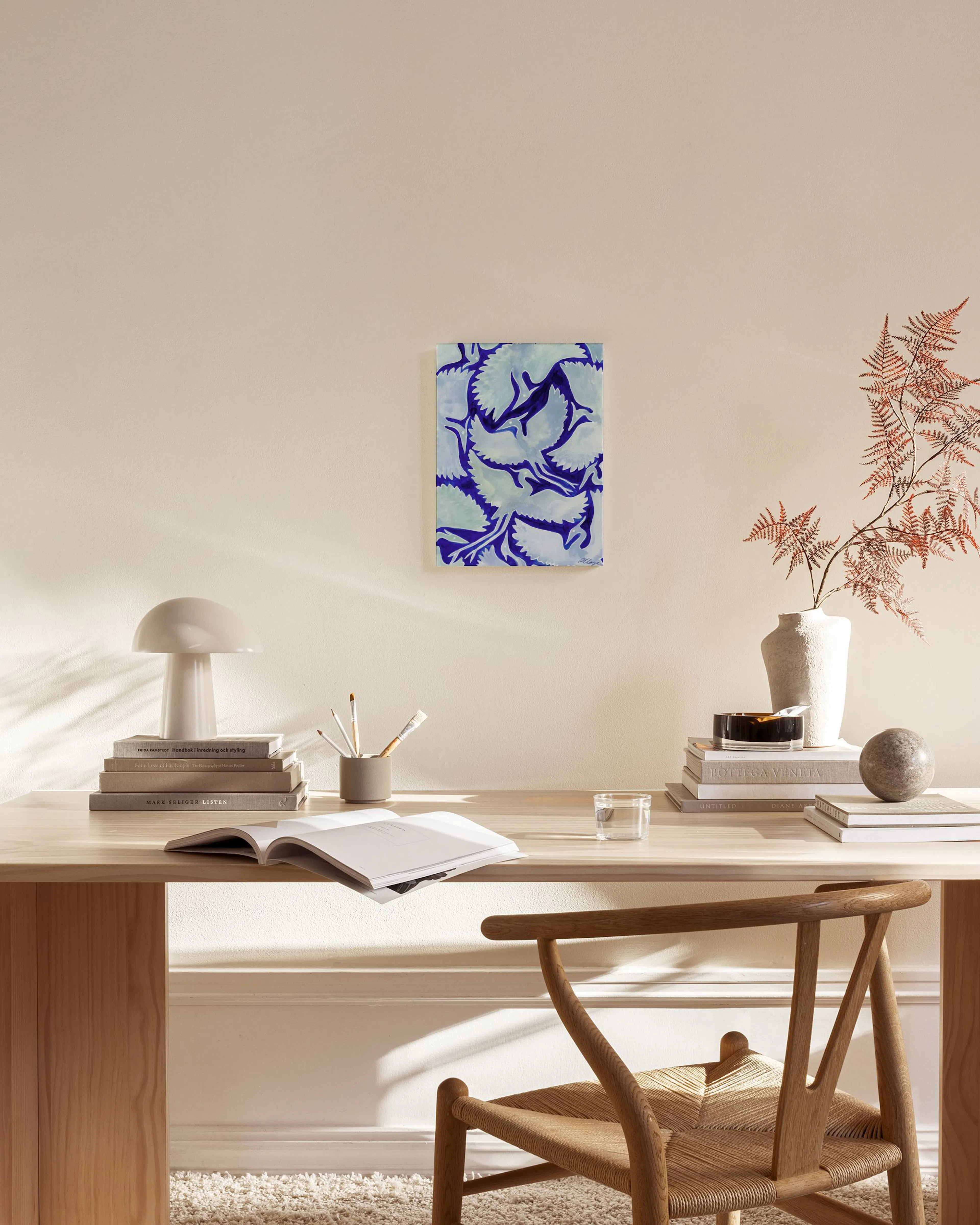 Tela decorativa com padrão abstrato de folhas em tons de azul e lilás, exibida numa sala de estar minimalista acima de um móvel 