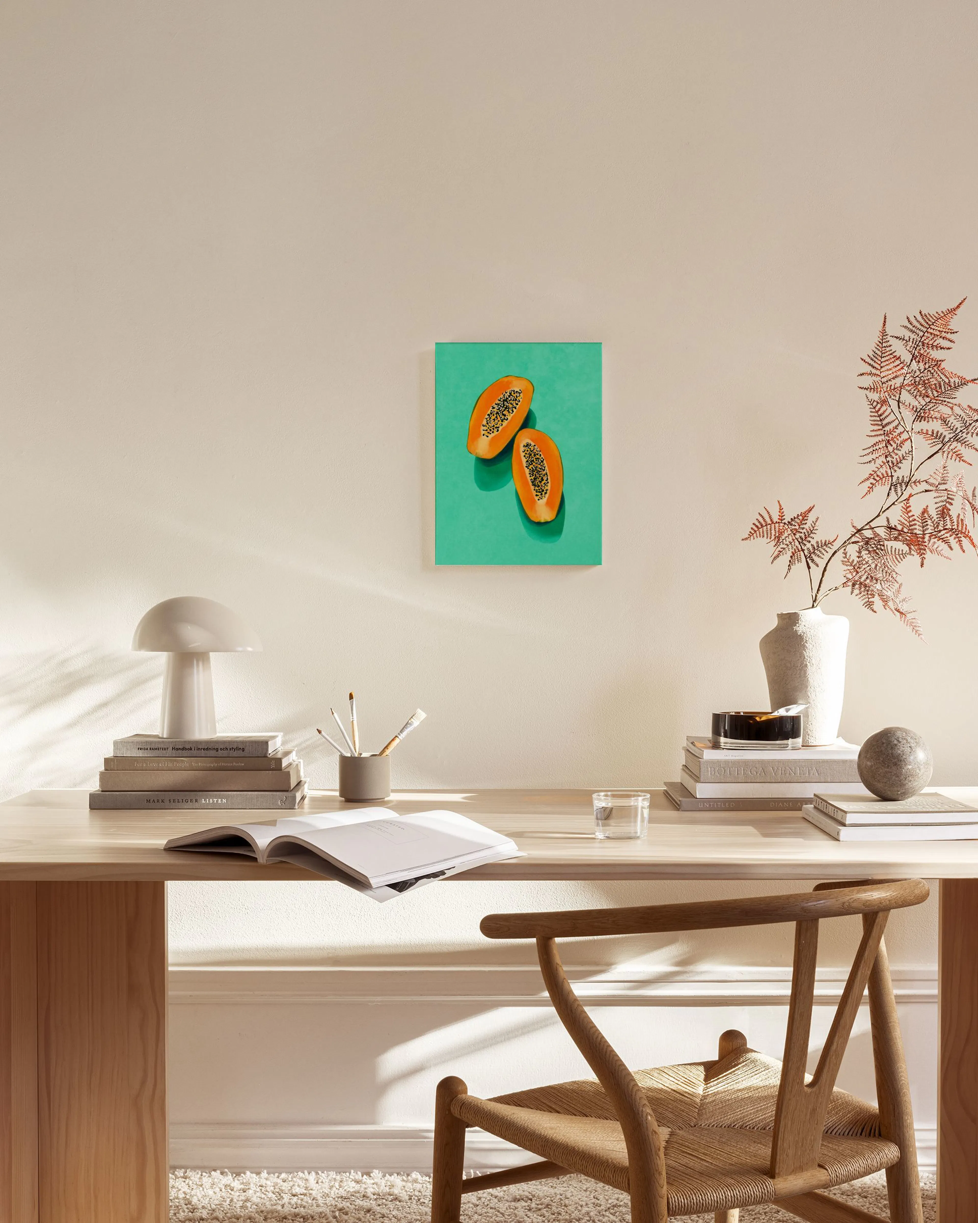 A bright canvas print of two papaya halves on a teal background, hanging above a console table in a minimalist living room.