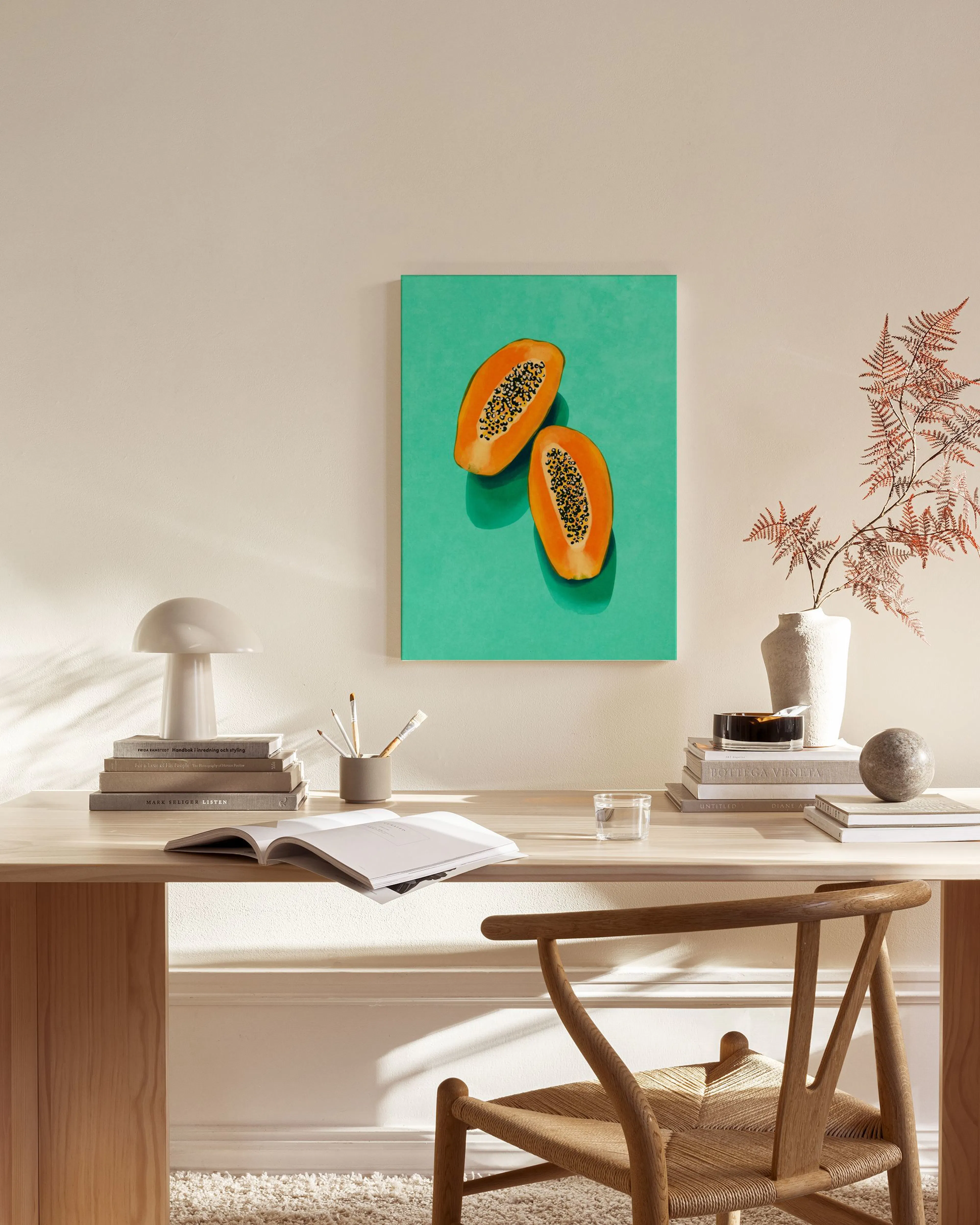 A colorful canvas print of two halved papayas on a bright green background, hanging in a modern living room above a wooden conso