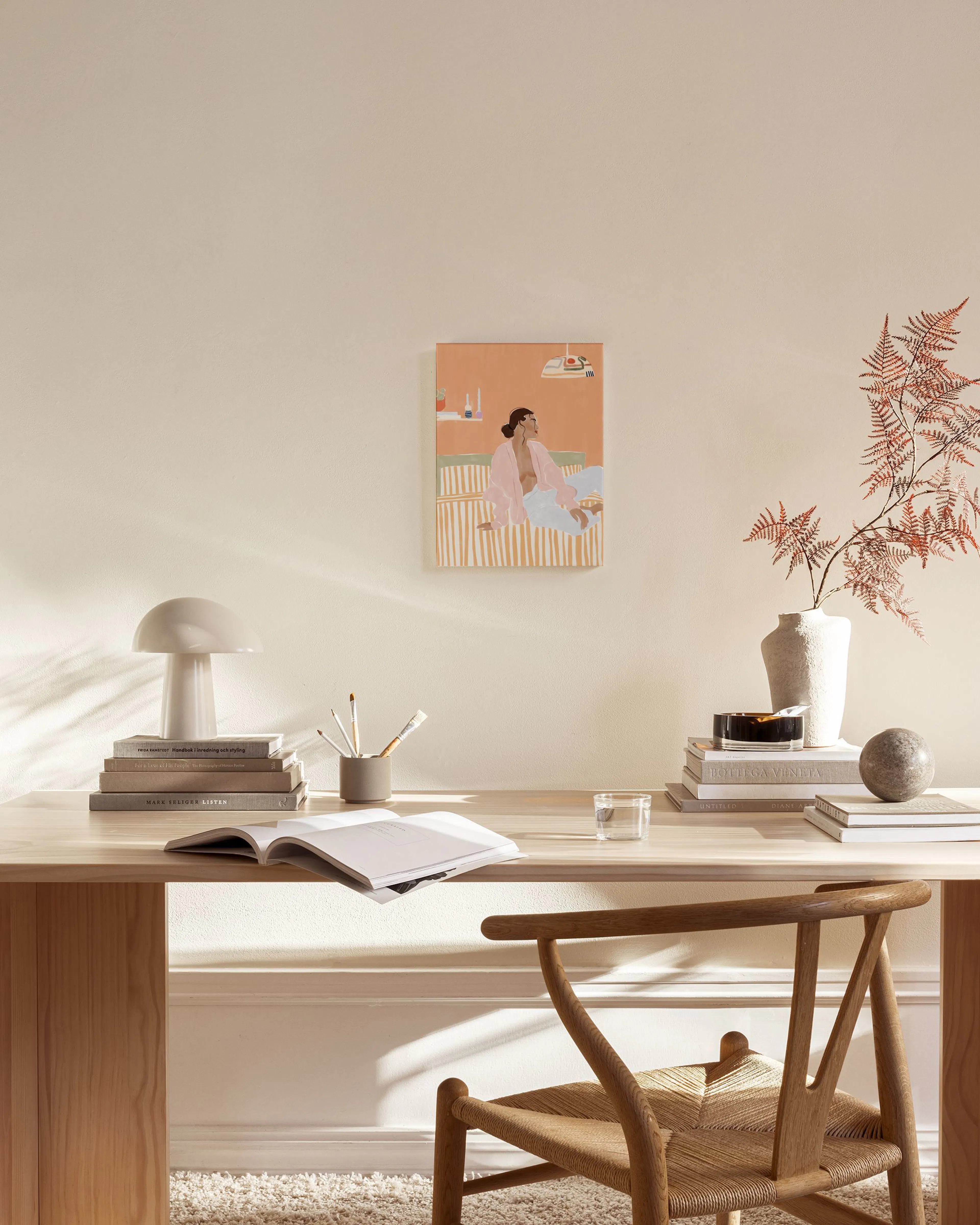 Art print of a woman in pink and blue clothing sitting on a striped bed, displayed in a light-filled living room.