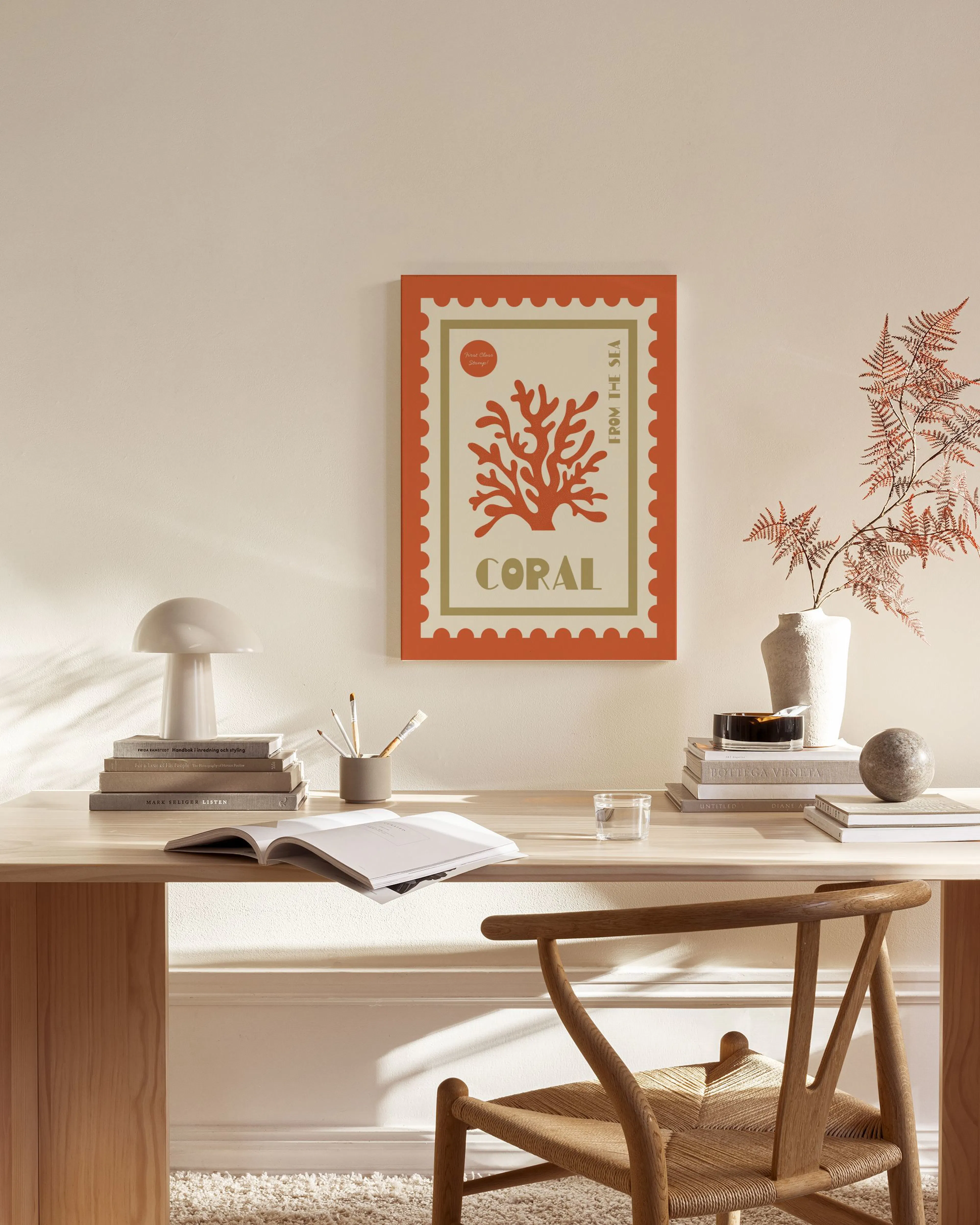 A coral reef stamp print in red and gold, hanging above a wooden console table in a neutral-toned living room.