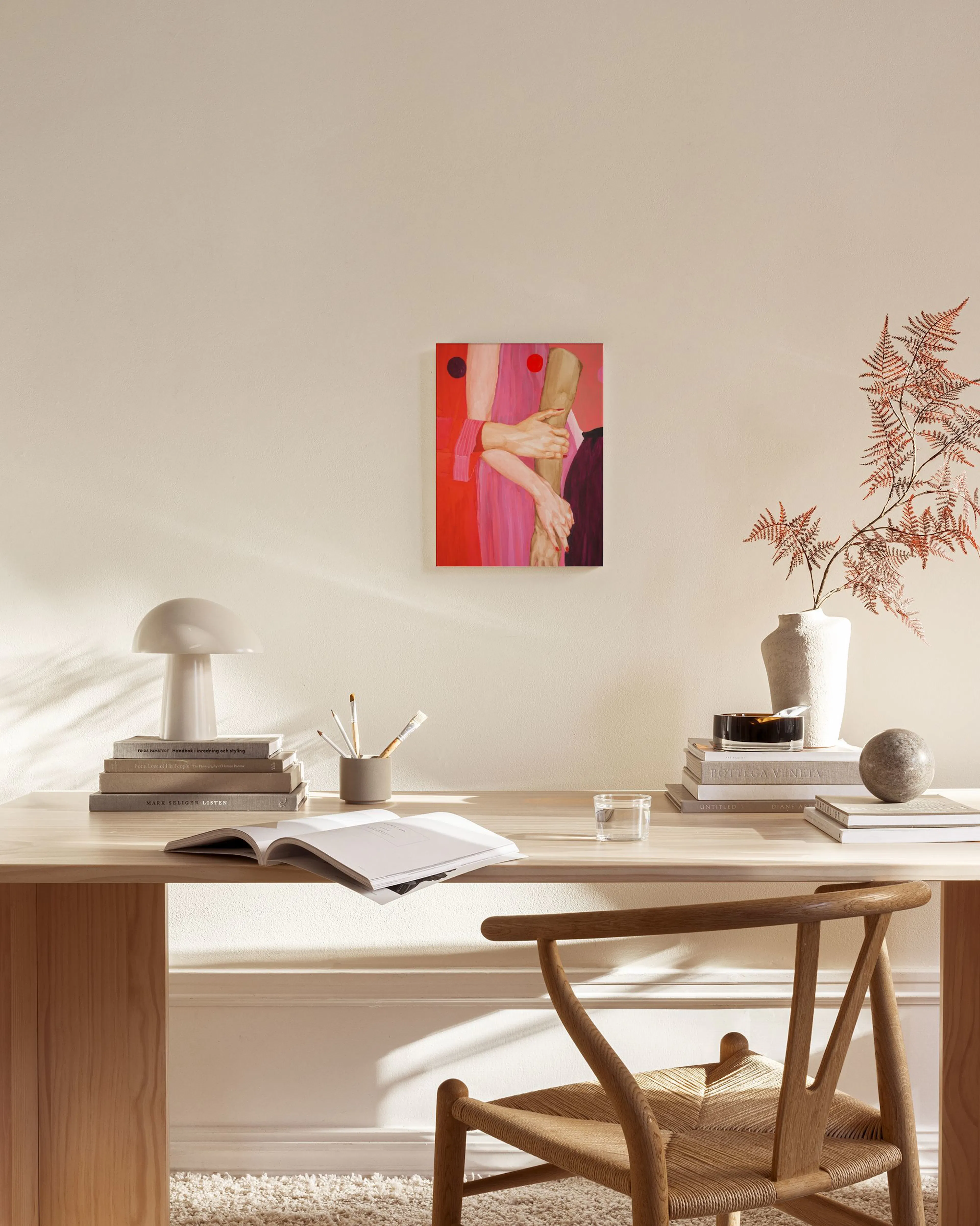 Canvas met roze en rode tinten, twee in elkaar grijpende handen en rode, zwarte cirkels, hangend in een lichte woonkamer.