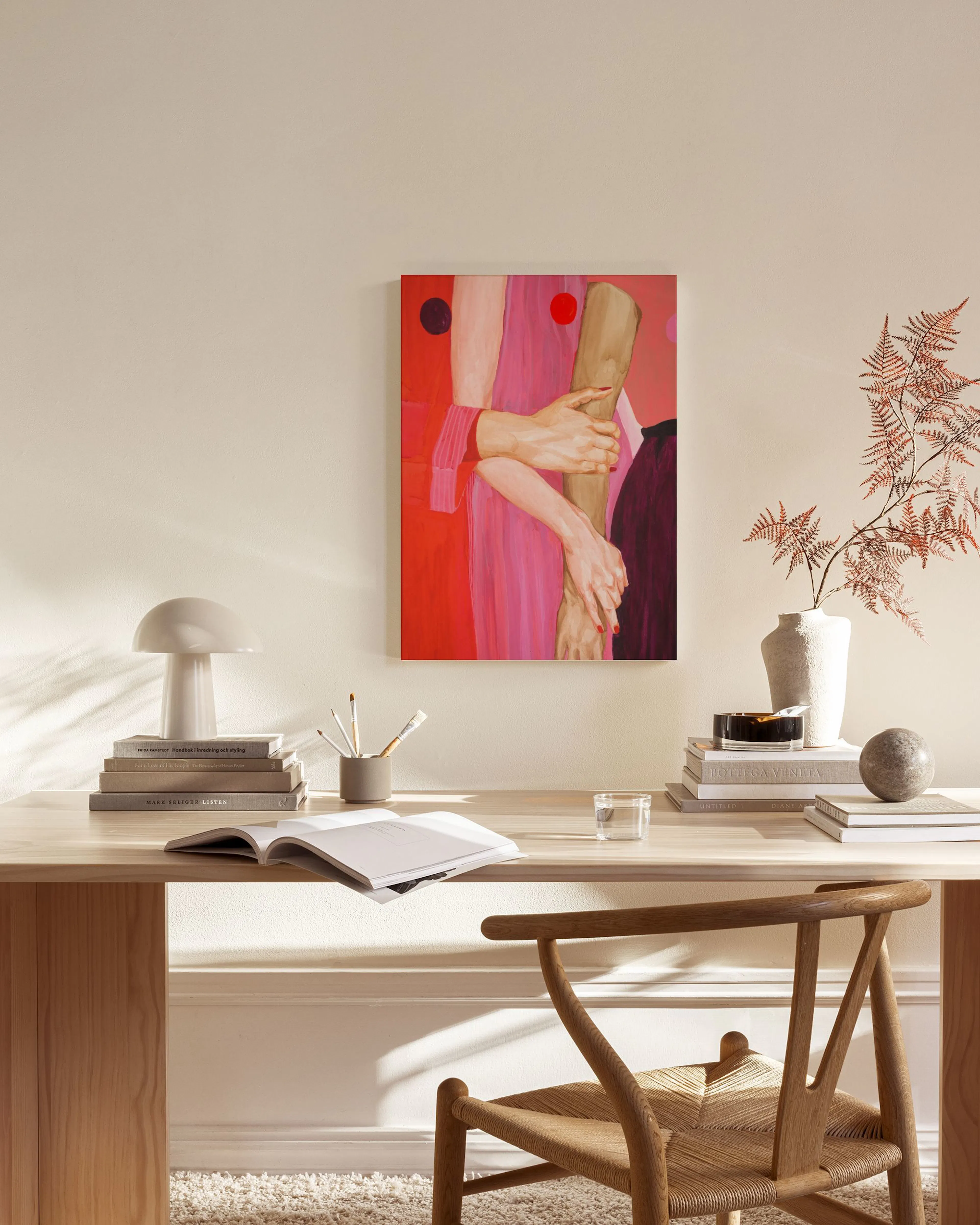 A canvas print of hands embracing a cylindrical object, with red and pink clothing, hanging in a minimalist living room.