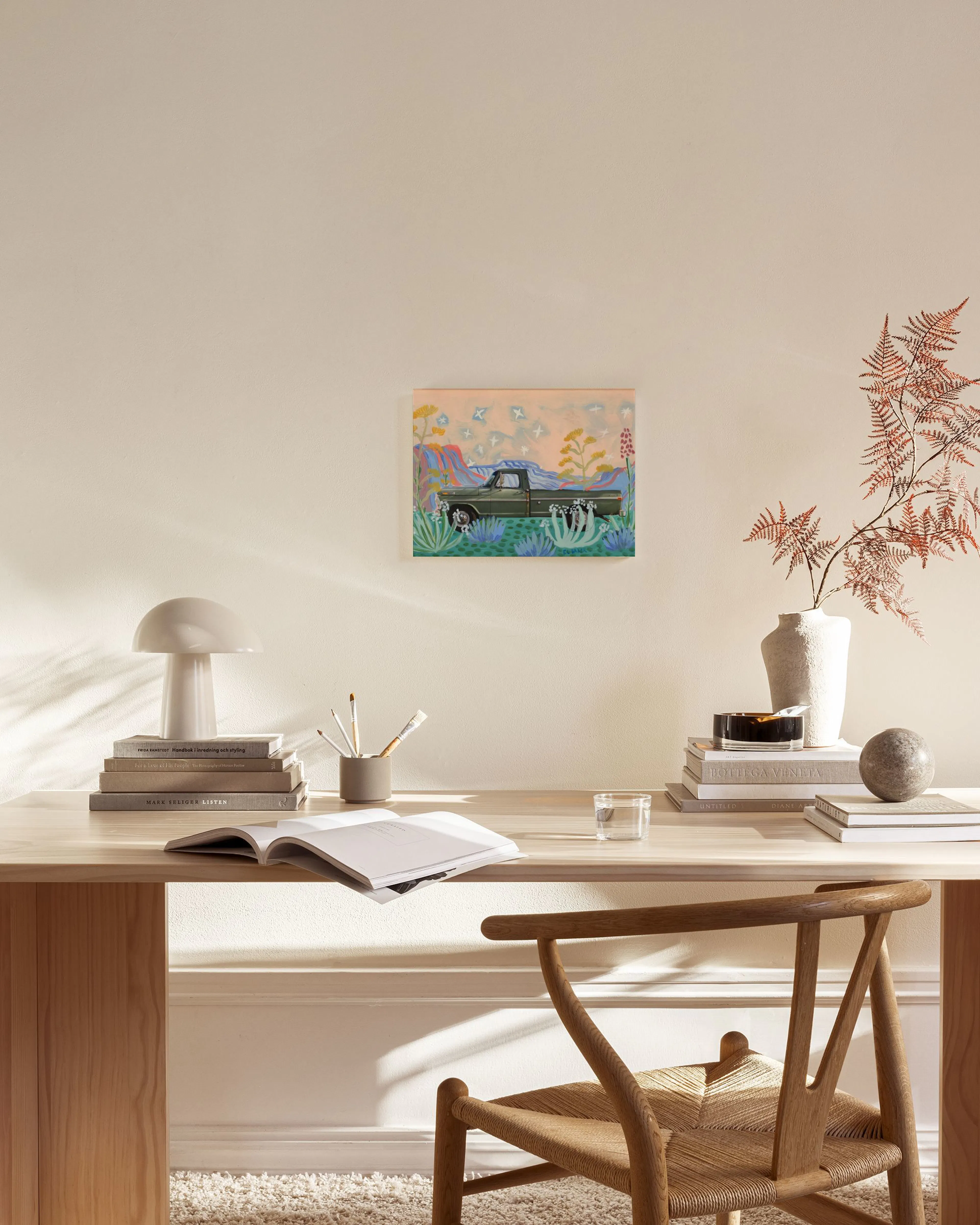 A colorful painting of a green pickup truck in a desert landscape with cacti and mountains, displayed in a modern living room.