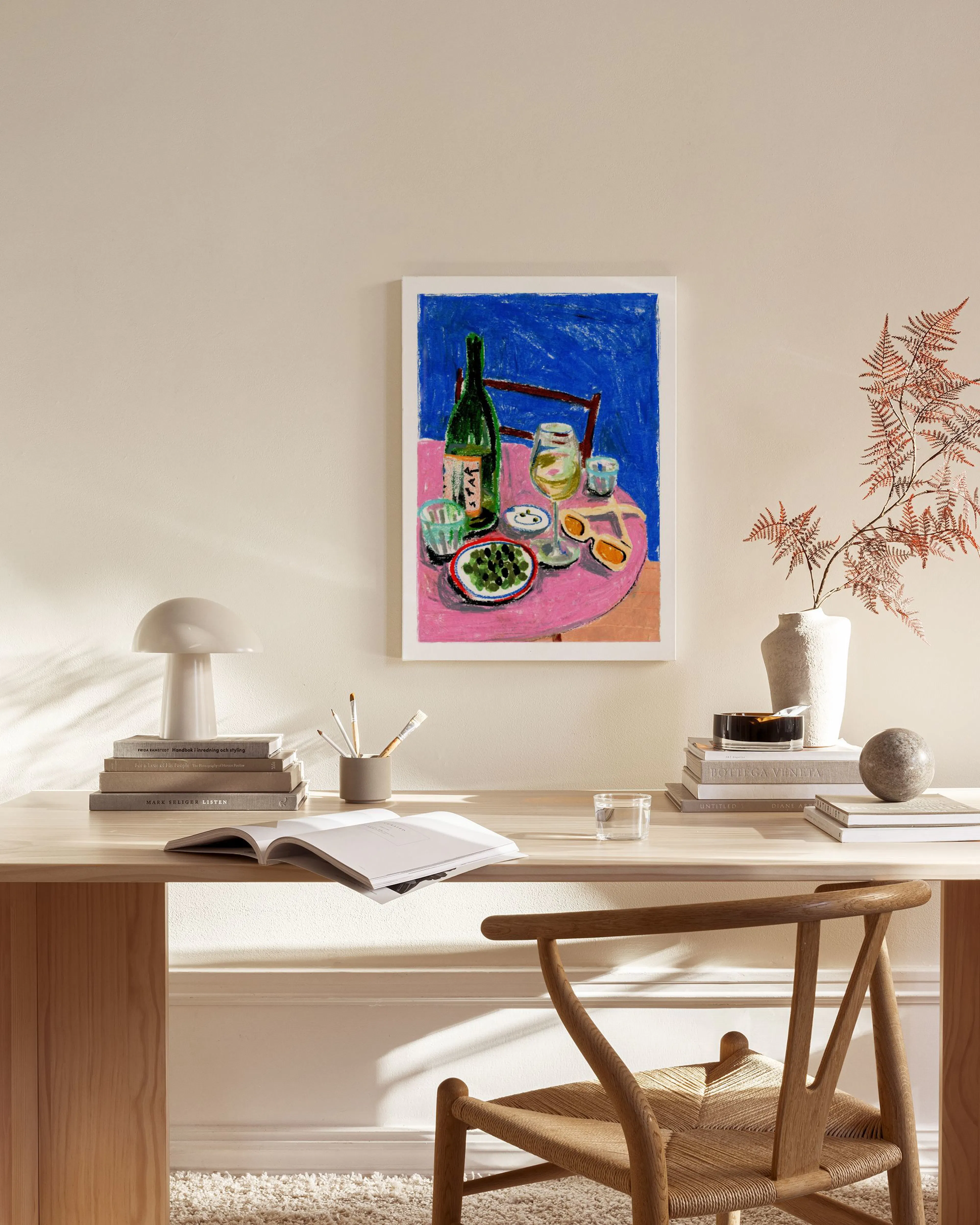A colorful still life painting of a wine bottle, glasses, and olives on a pink table, displayed in a modern living room.