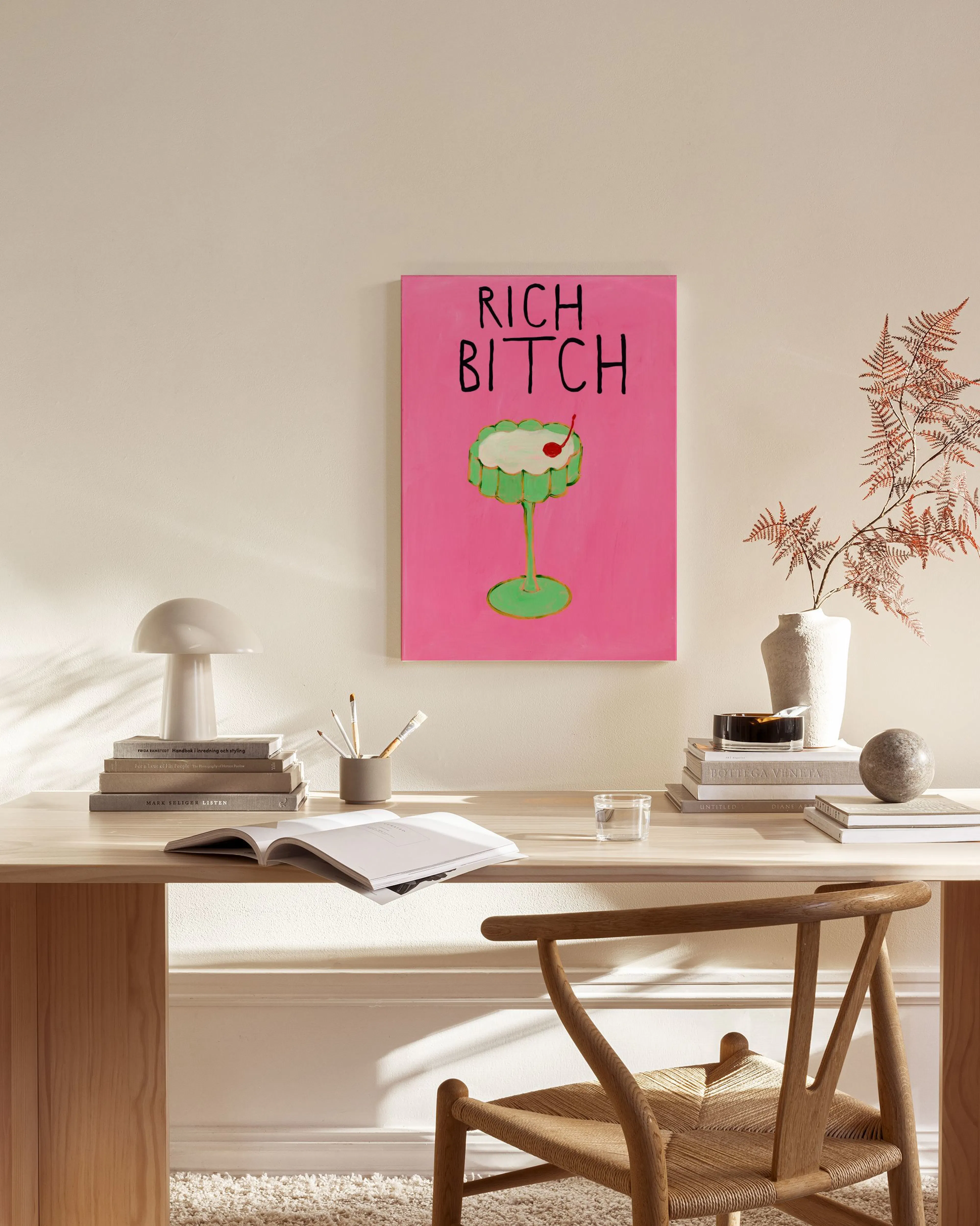 A vibrant pink canvas print of a green cocktail glass with a cherry and the words RICH BITCH in black, hanging in a minimalist l