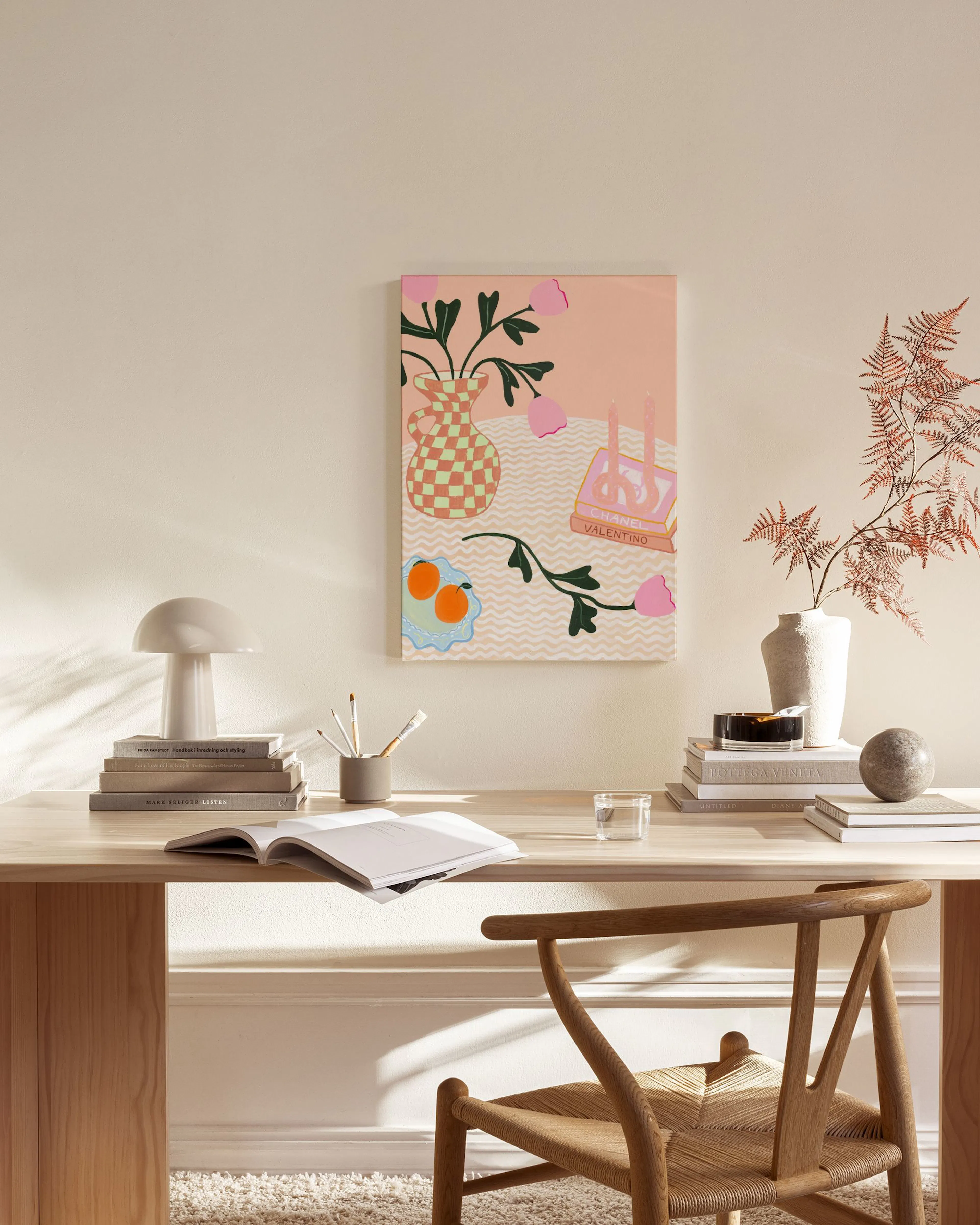 Canvas met roze bloemen in een geruite vaas en sinaasappels, hangend boven een houten dressoir in een moderne woonkamer.