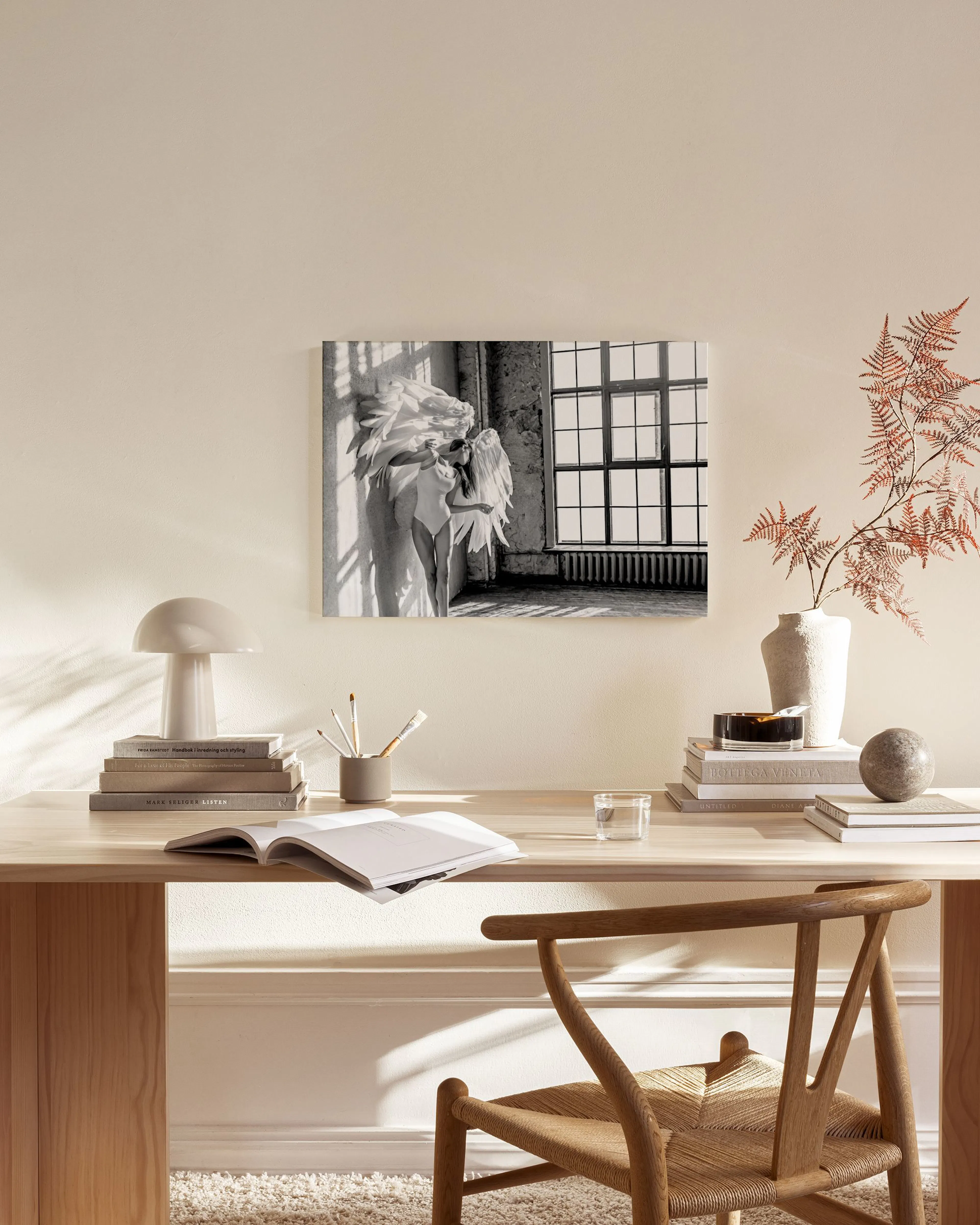 Black and white canvas print of a woman with large angel wings, bathed in sunlight, hanging in a minimalist living room.