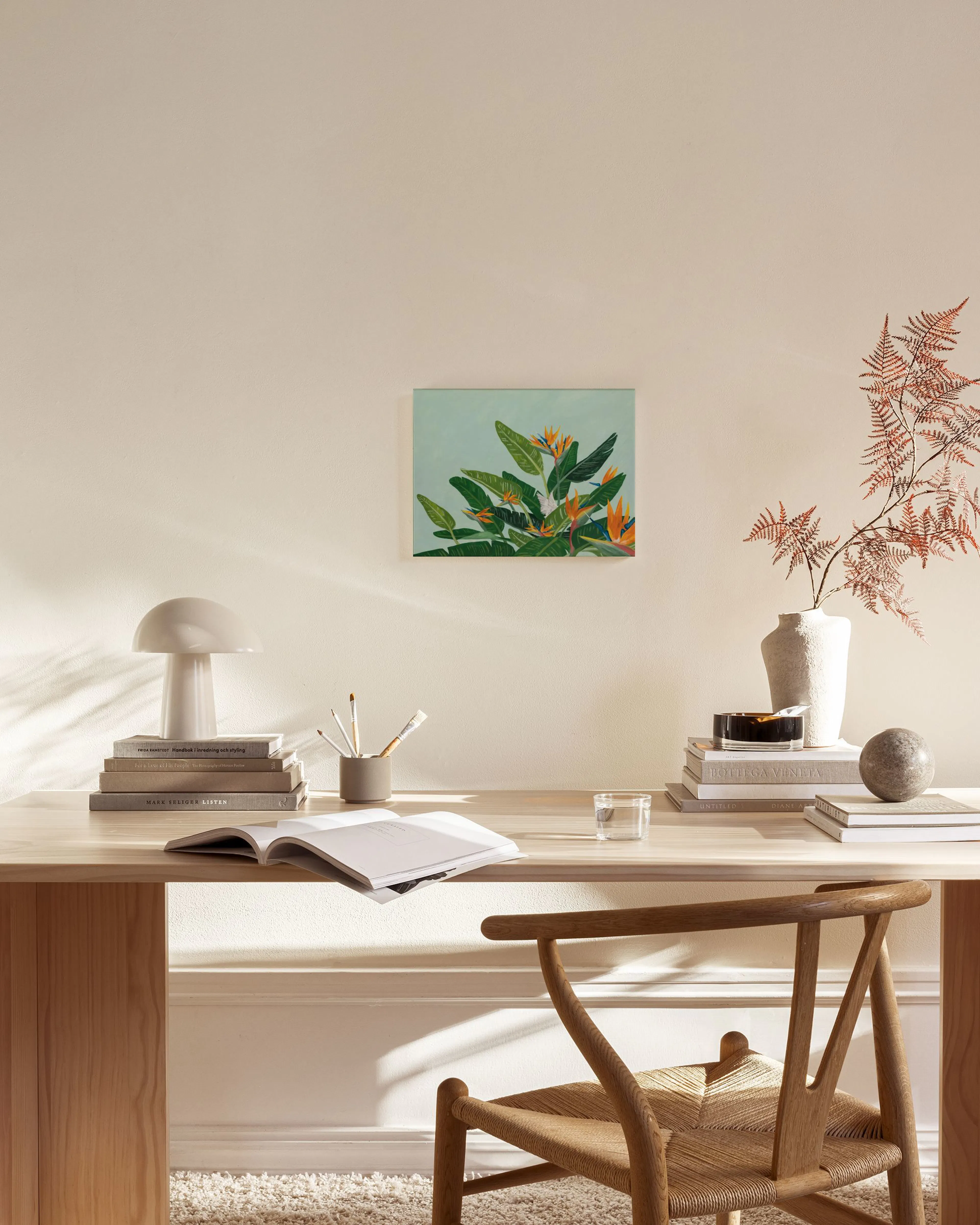 Canvas print of lush green leaves and orange bird of paradise flowers, hanging in a bright, minimalist living room.