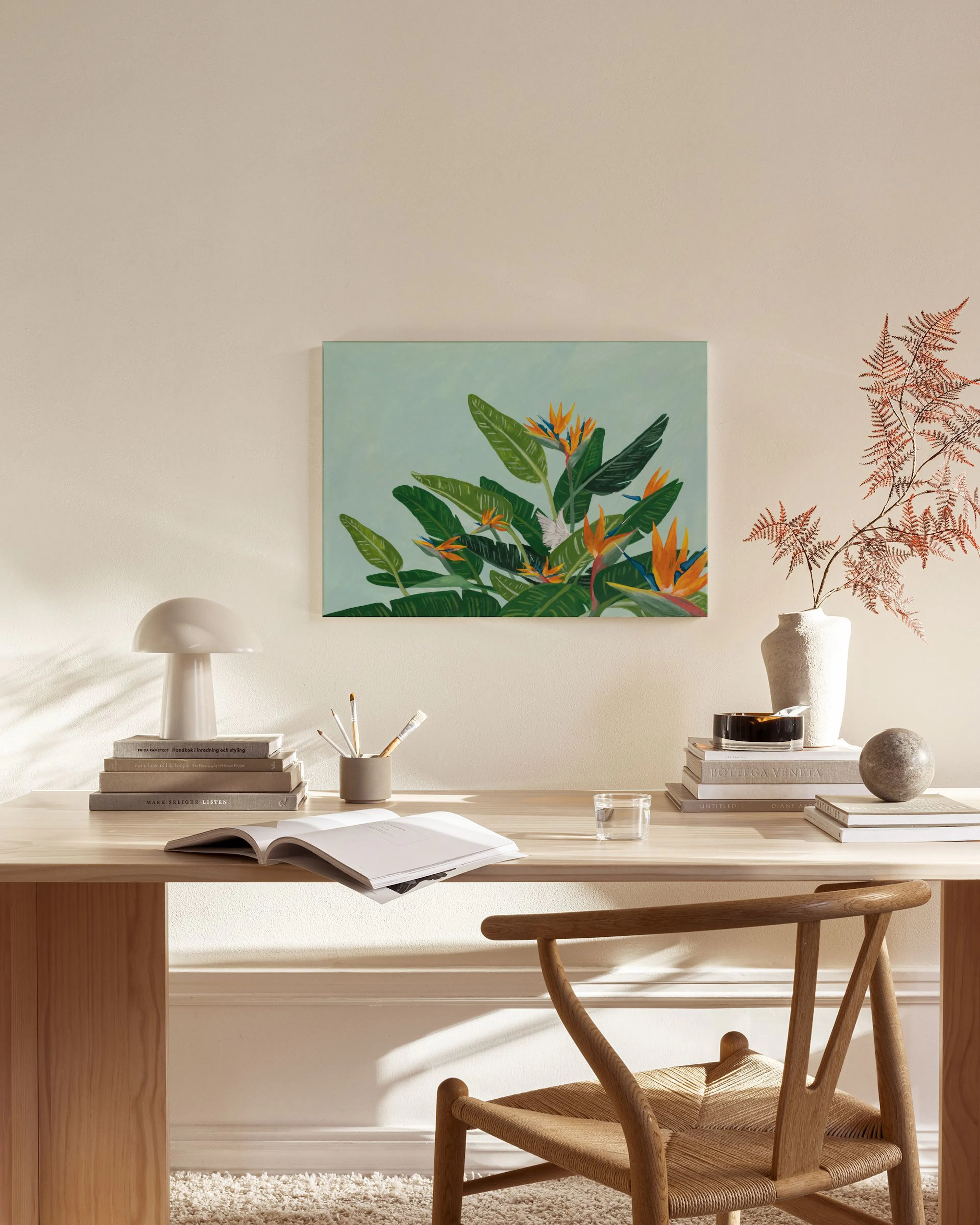 Canvas met oranje paradijsvogelbloemen en groene bladeren op een lichtblauwe achtergrond, hangend in een neutrale woonkamer.