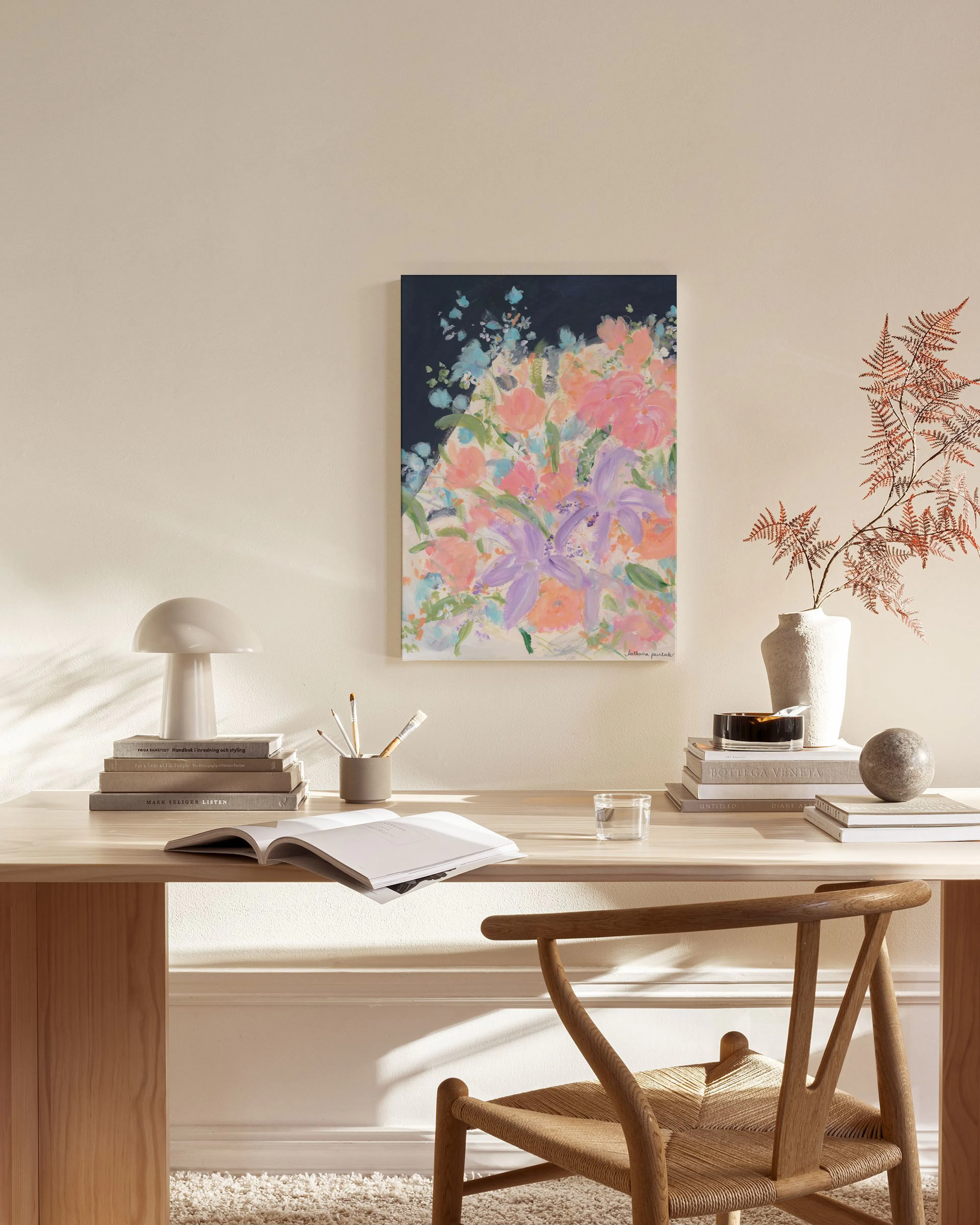 A vibrant floral print with pink, peach, and purple flowers on a dark blue background, hanging above a wooden console table in a