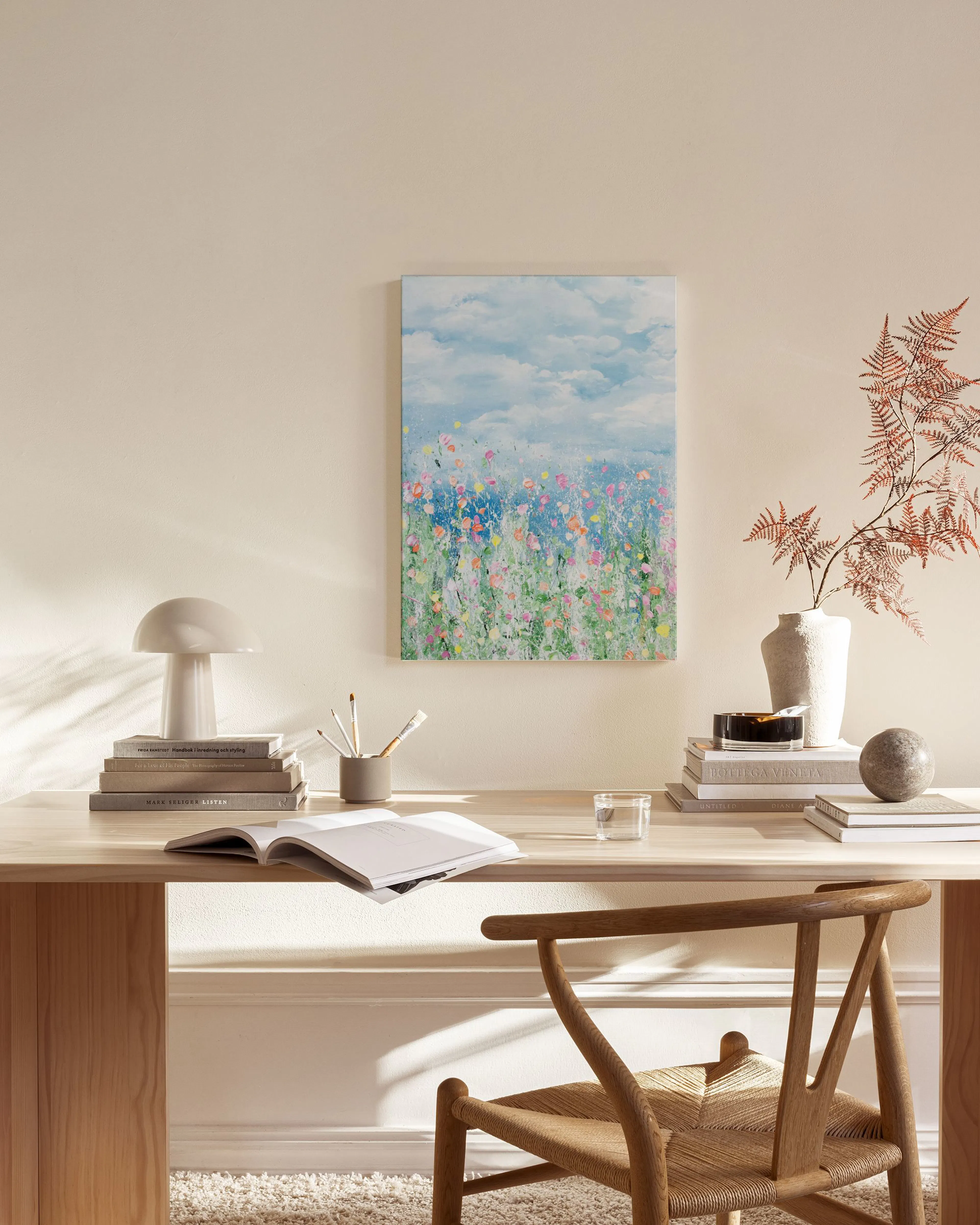 A canvas print of a vibrant wildflower field under a blue sky with clouds, displayed in a bright living room above a wooden cons