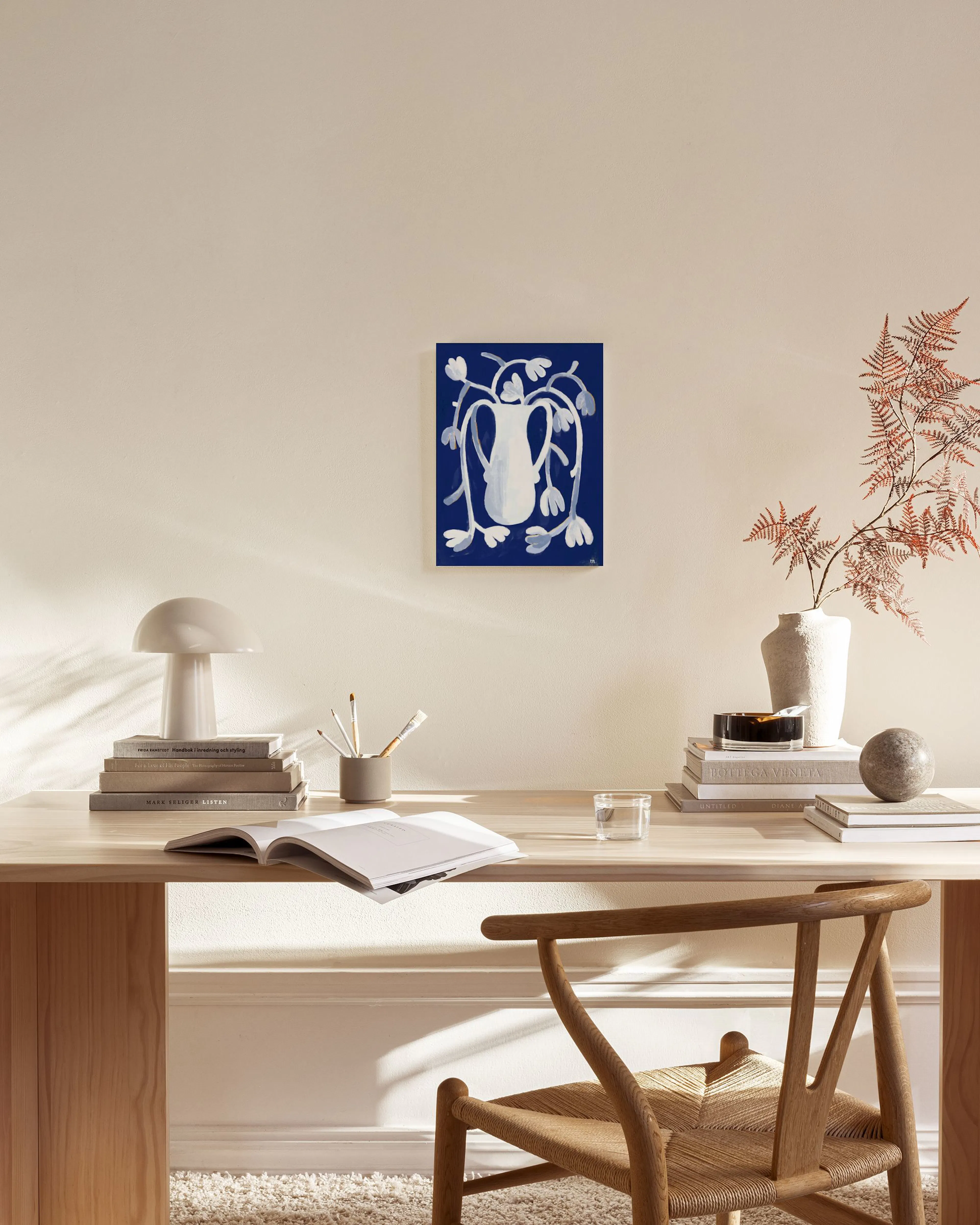 Lienzo abstracto azul con un jarrón blanco y follaje, colgado en una sala de estar moderna.