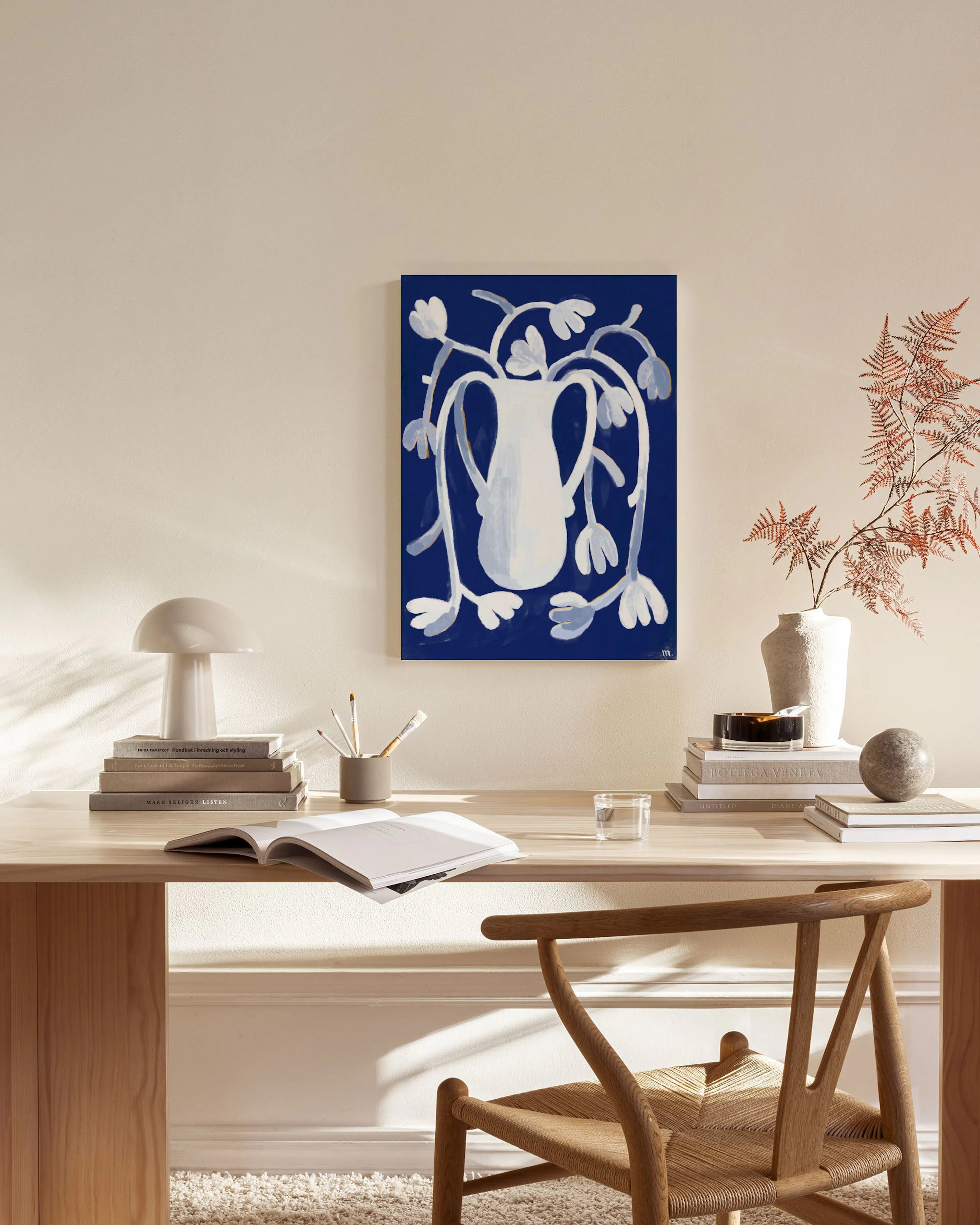 A canvas print with a white vase and light blue flowing floral elements on a deep blue background, displayed in a modern living 
