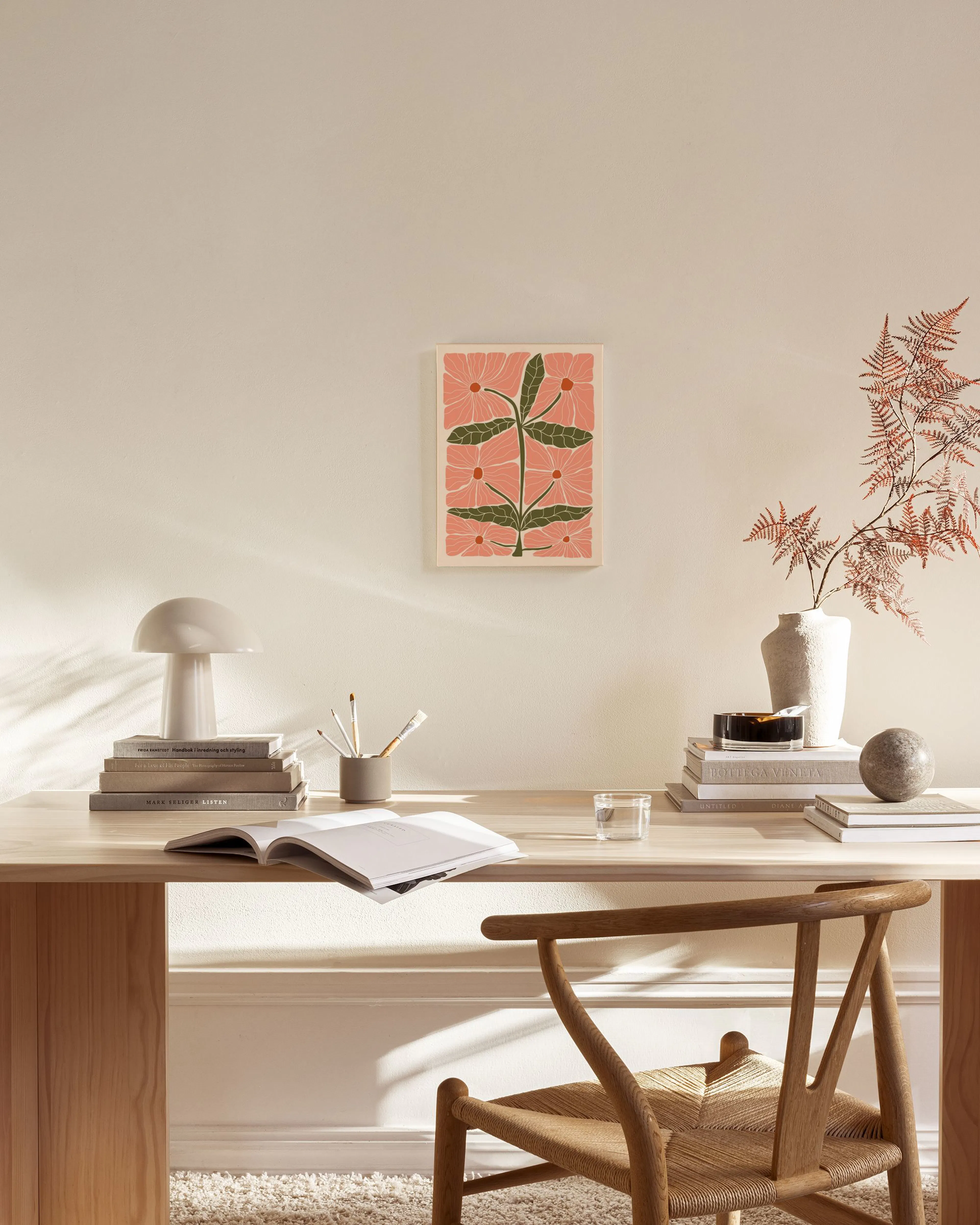 A canvas print of pink flowers with green leaves on a cream background, hanging above a wooden console table in a minimalist liv