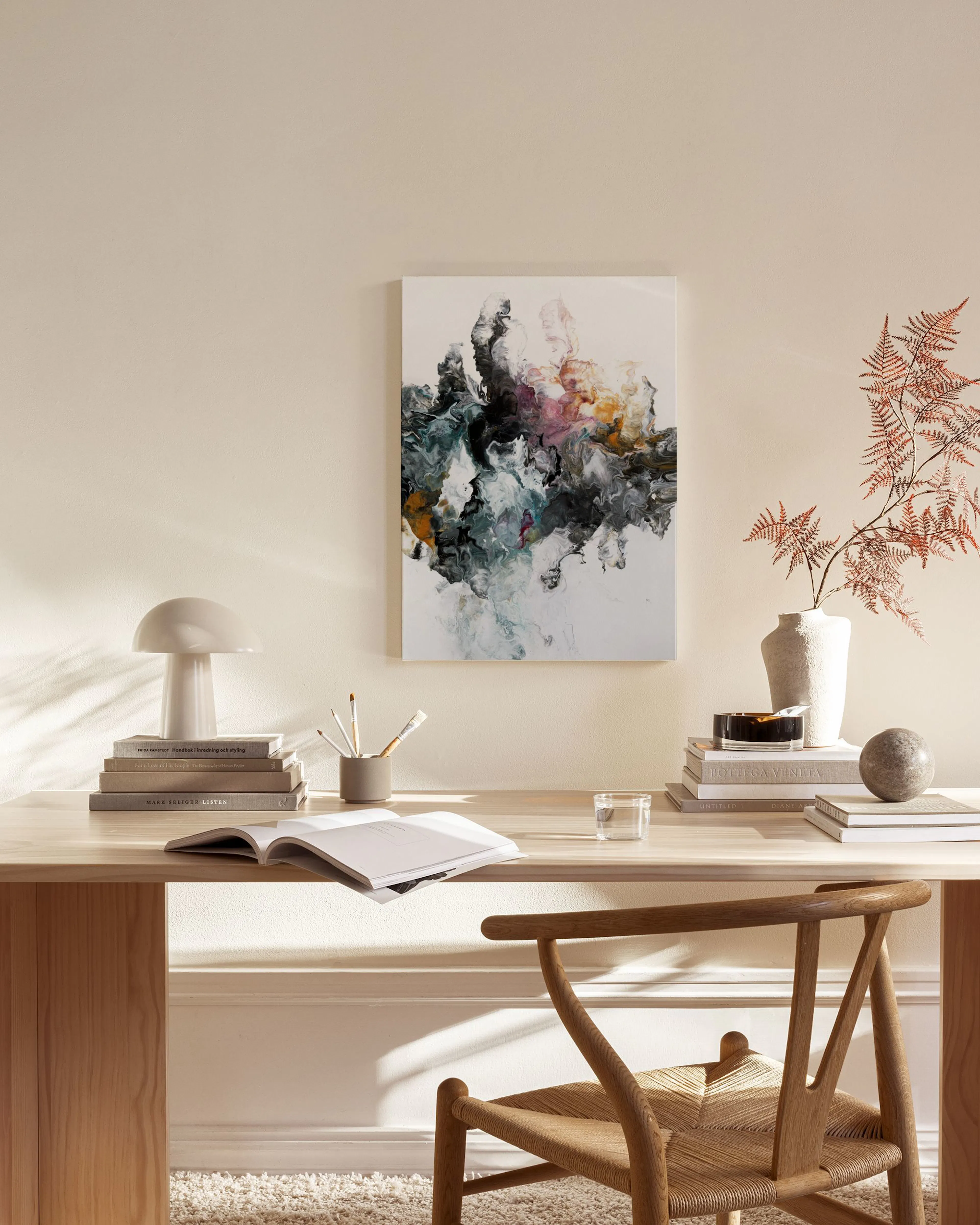 An abstract canvas print with organic dark gray, teal, pink, and ochre shapes, displayed in a minimal living room.