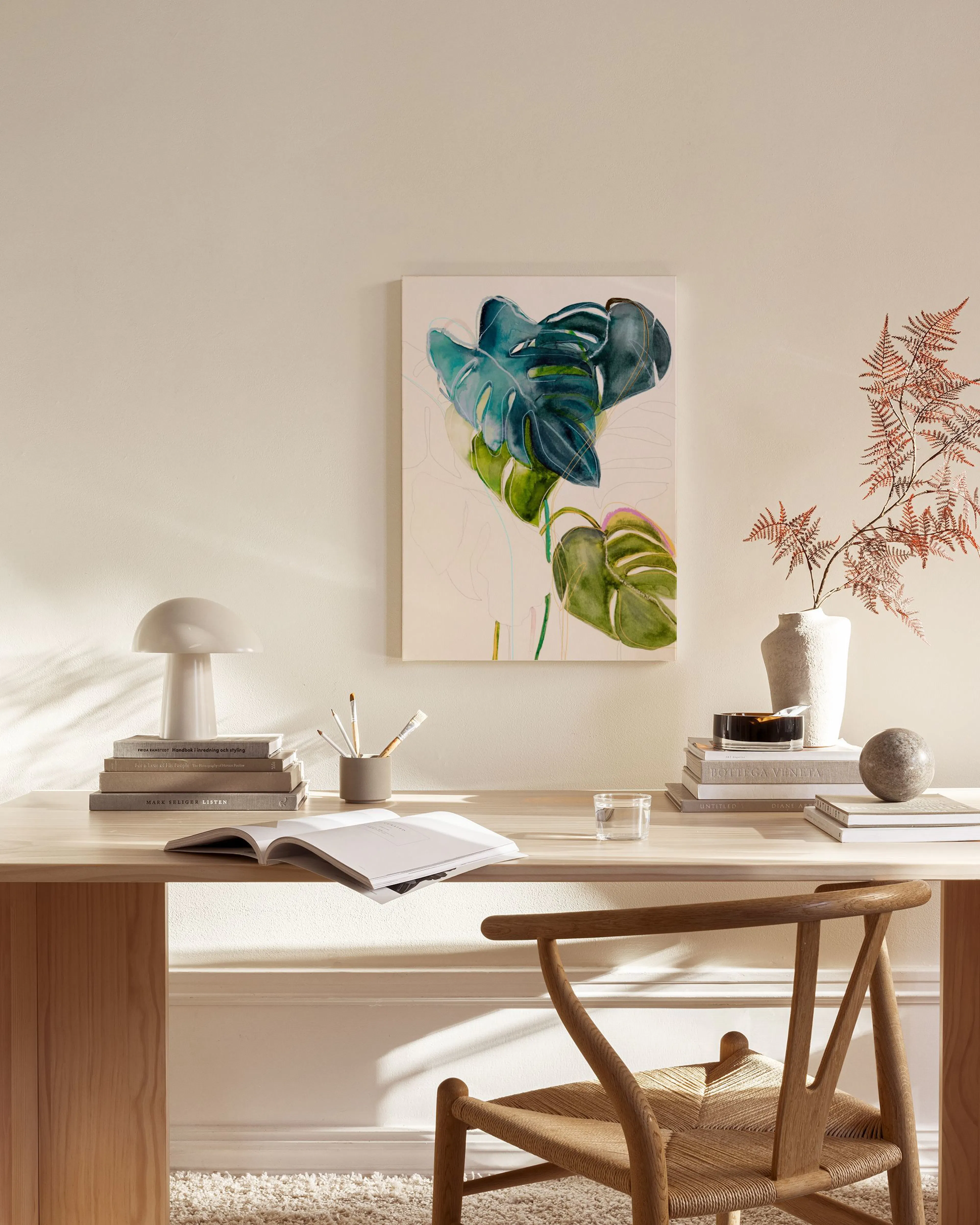 A canvas print of a large green and blue monstera leaf, with lighter green leaves below, hanging in a light-filled living room.