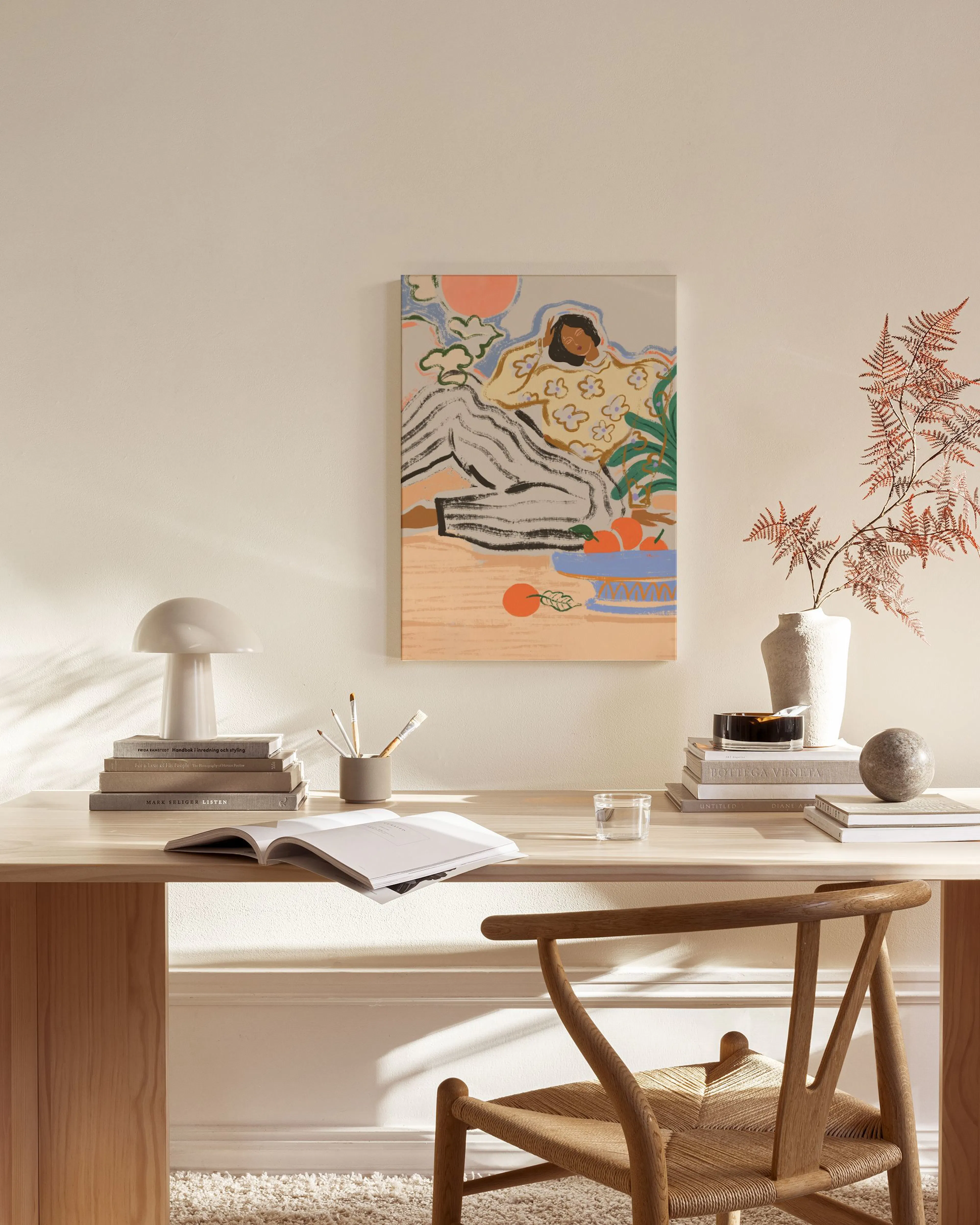 Lienzo con ilustración de persona sentada, con un cuenco de naranjas, en tonos pastel, colgado sobre un mueble bajo de madera en