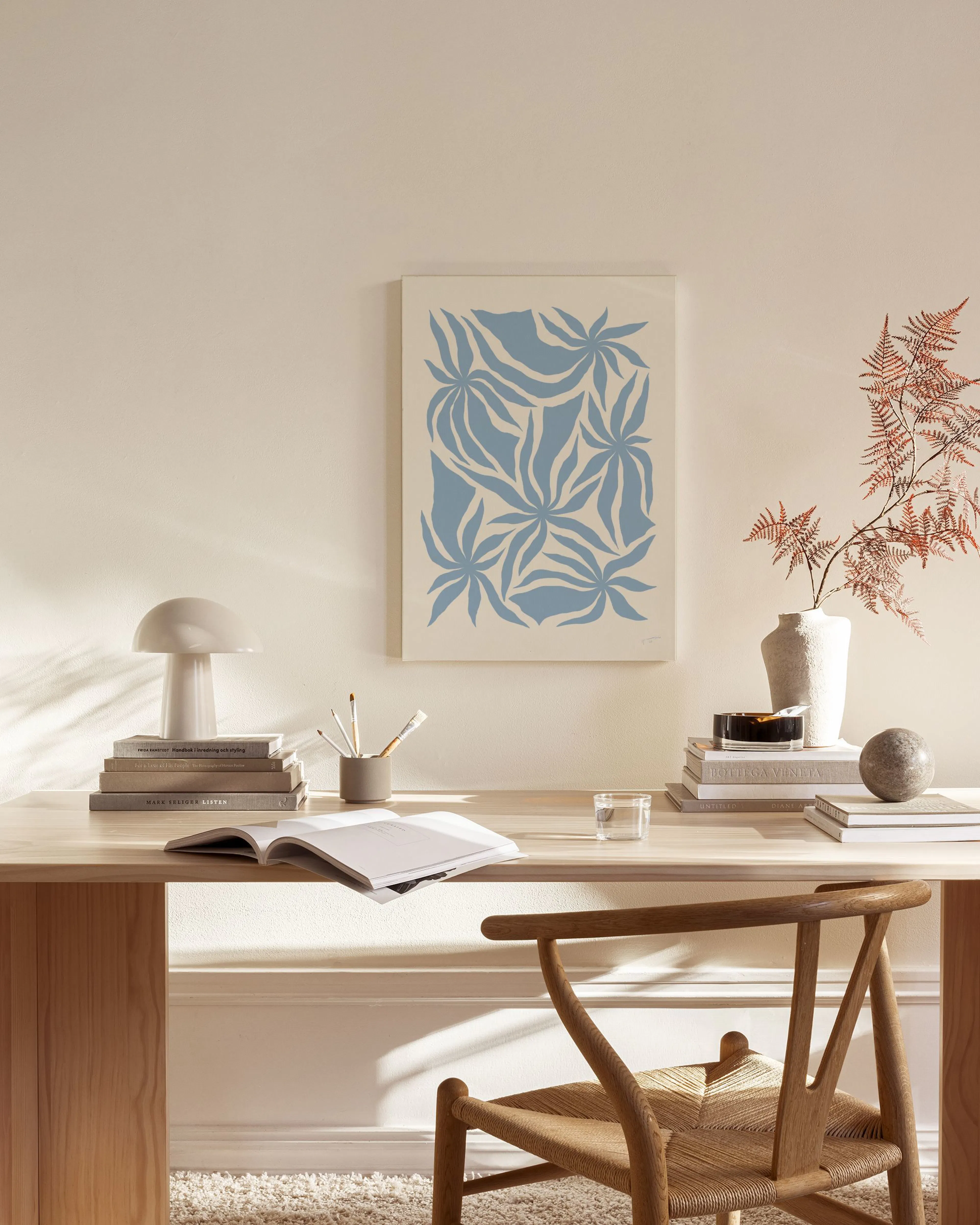 Botanical canvas print with light blue organic leaf shapes on a beige background, displayed on a light wall in a living room.