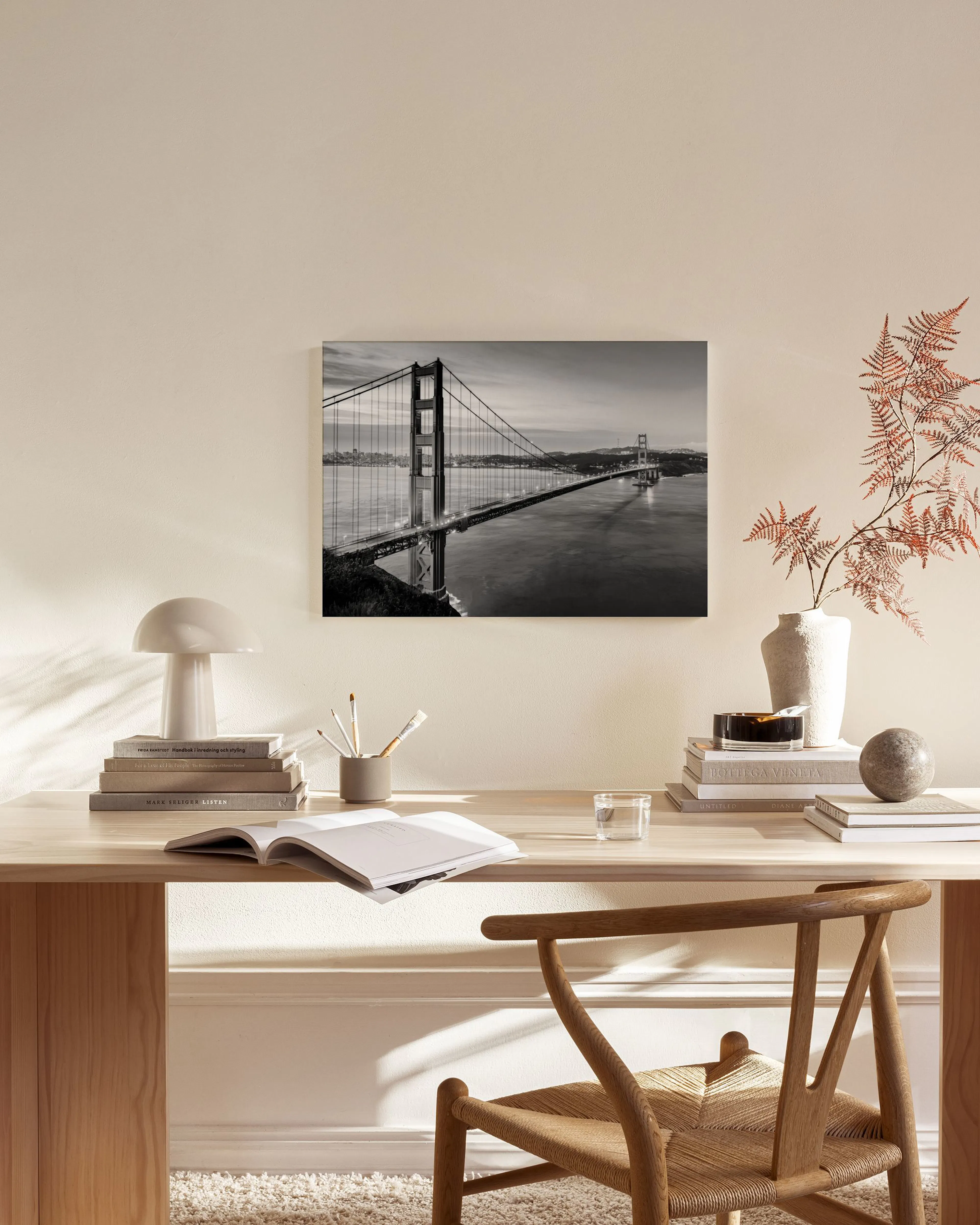 Zwart-wit canvas van de Golden Gate Bridge bij zonsondergang, hangend in een moderne woonkamer boven een houten dressoir.