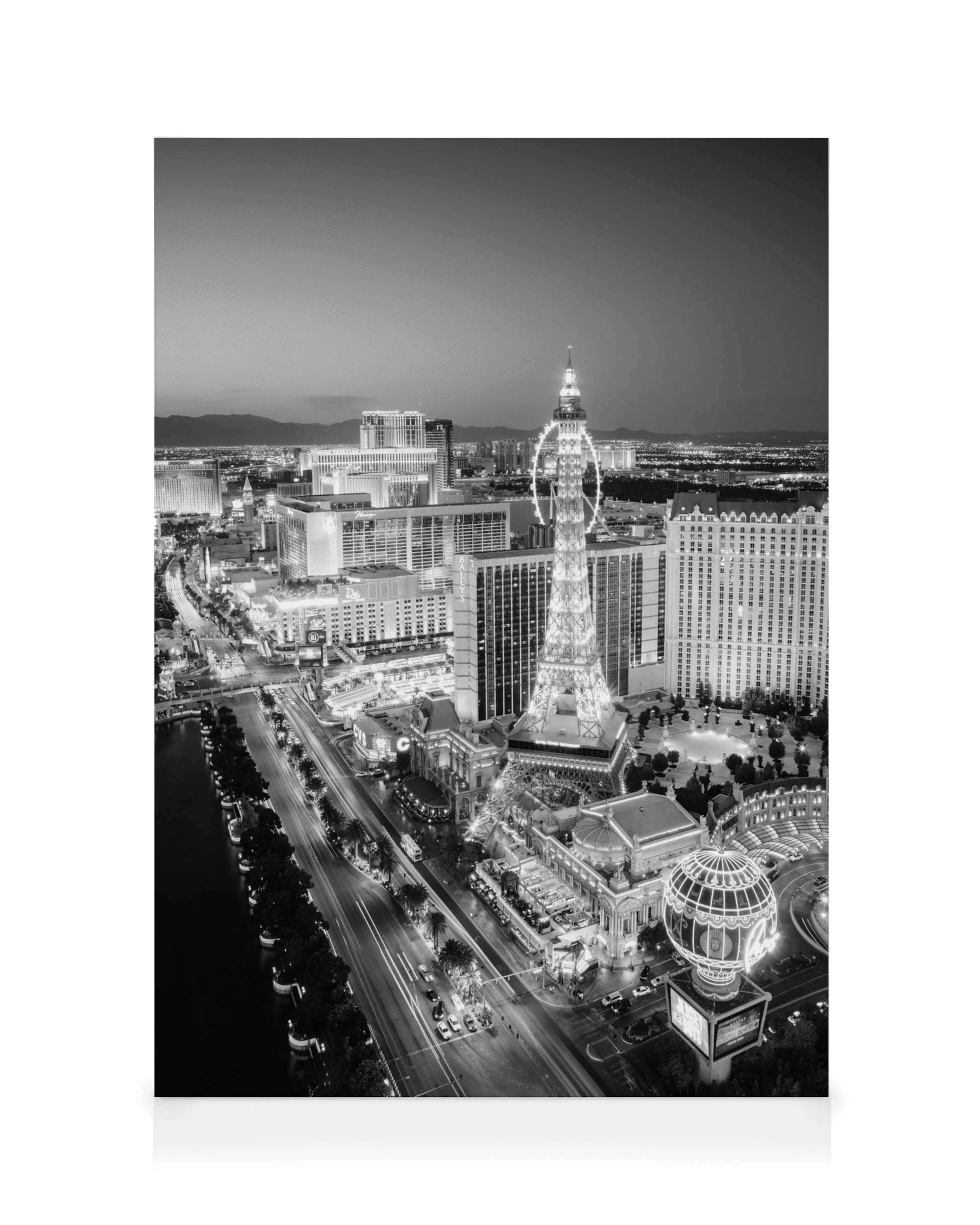 Black and white night view of the Las Vegas Strip, featuring the illuminated Eiffel Tower replica and bustling city lights.