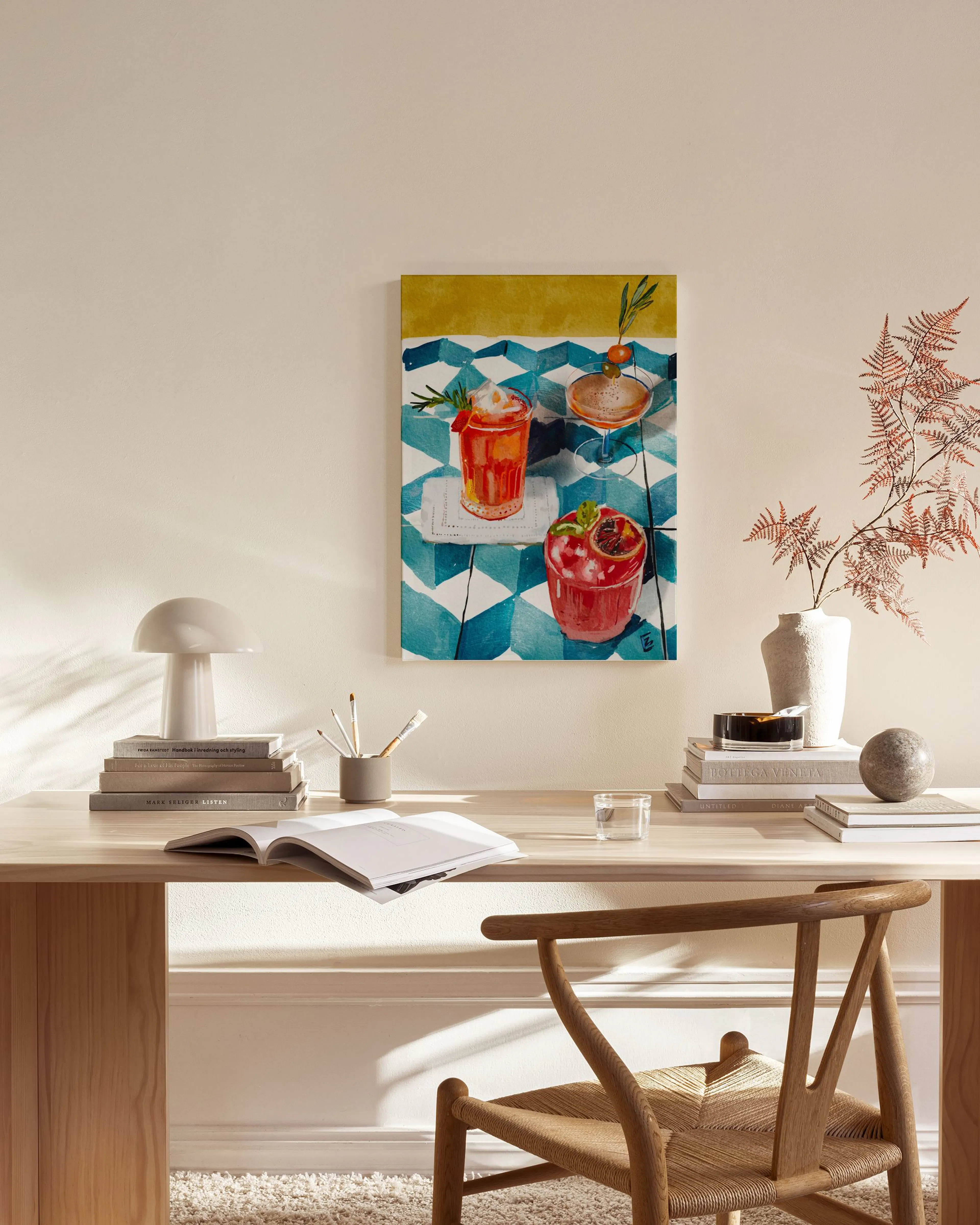 A canvas print of three vibrant cocktails on a blue and white checkered tablecloth, hanging in a minimalist living room.