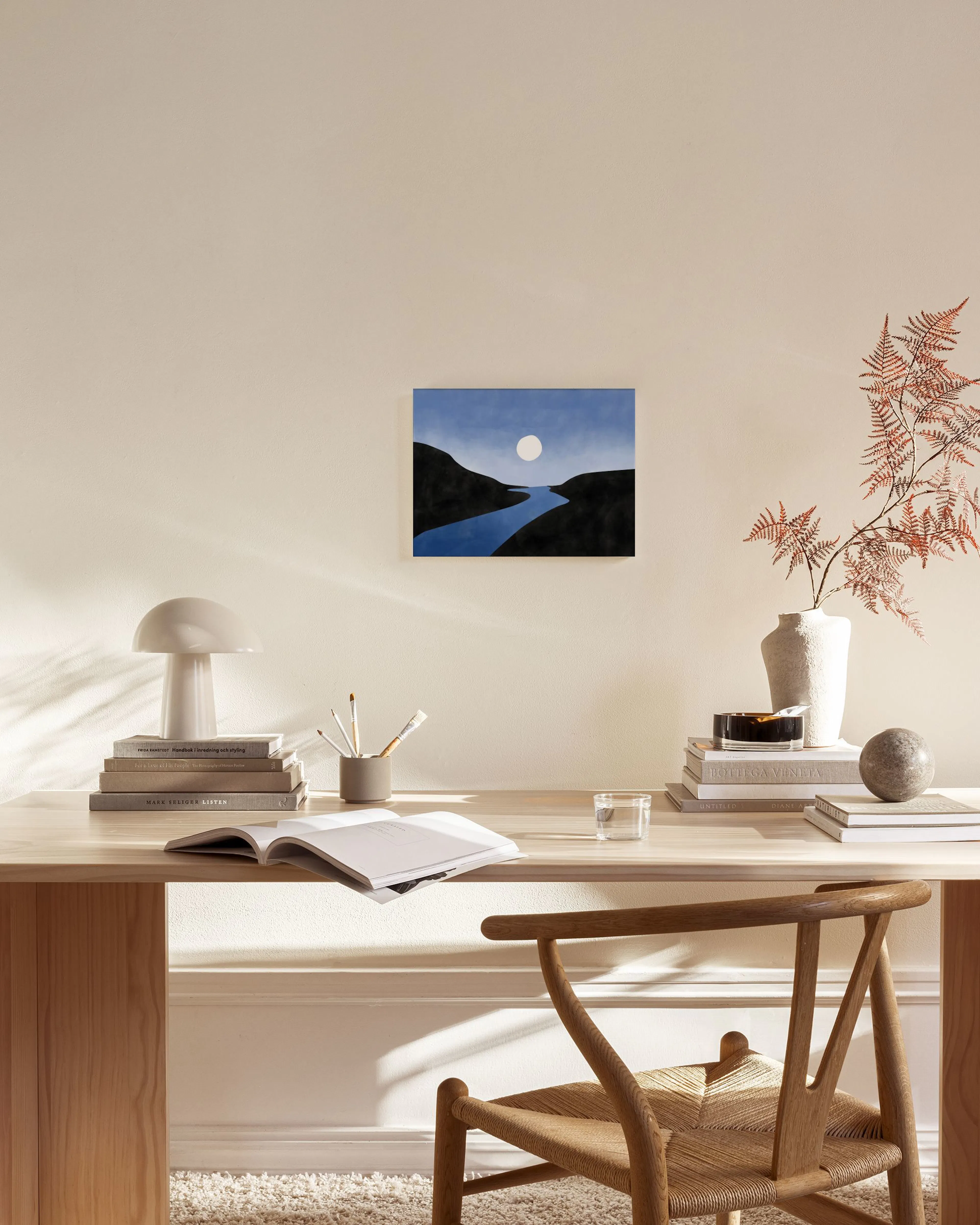 Leinwandbild mit blauem Fluss, schwarzen Hügeln und weißem Mond, in einem modernen Wohnzimmer über einem Sideboard.