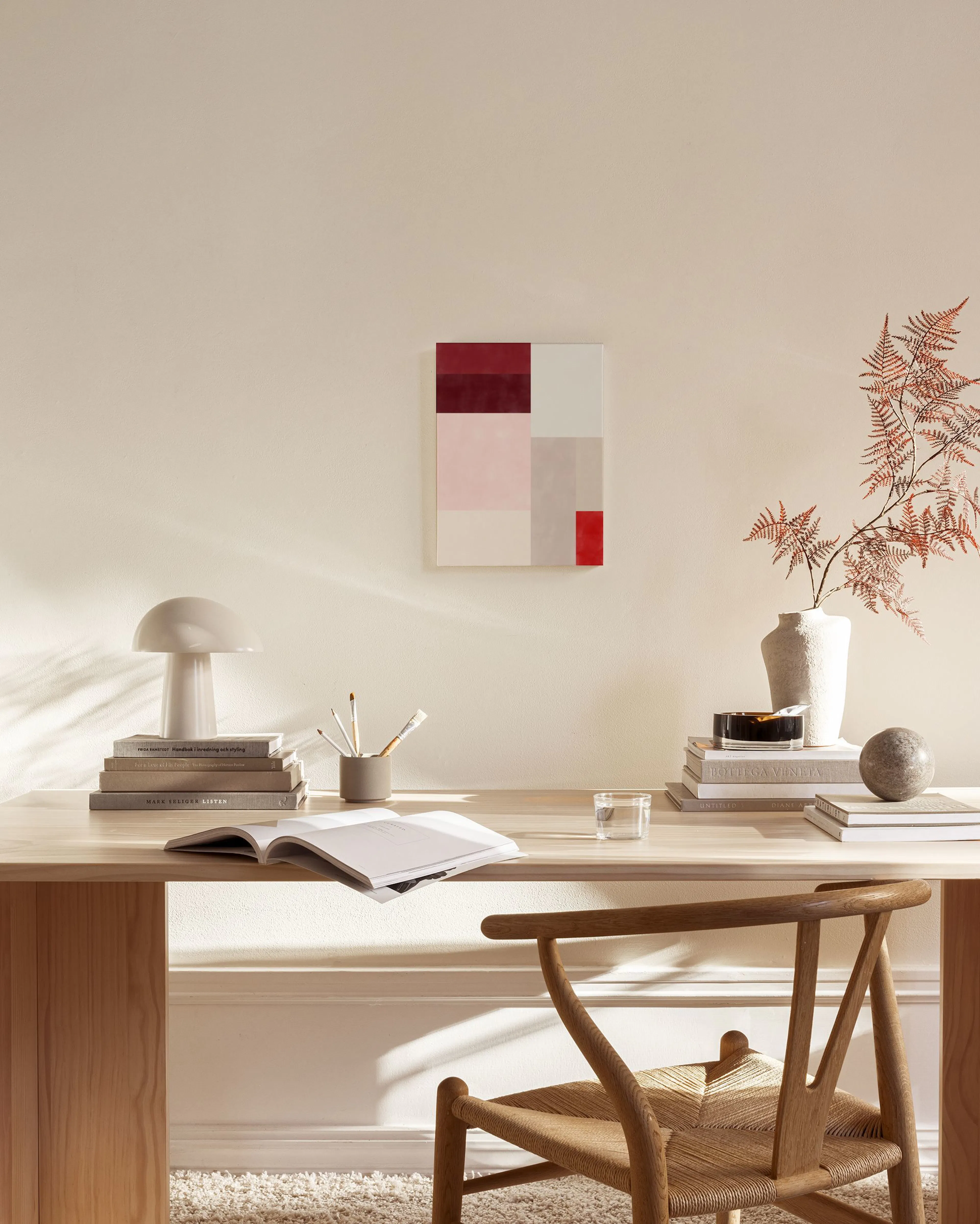 Toile aux formes géométriques rouges, roses et beiges, accrochée au-dessus dun meuble bas dans un salon moderne.