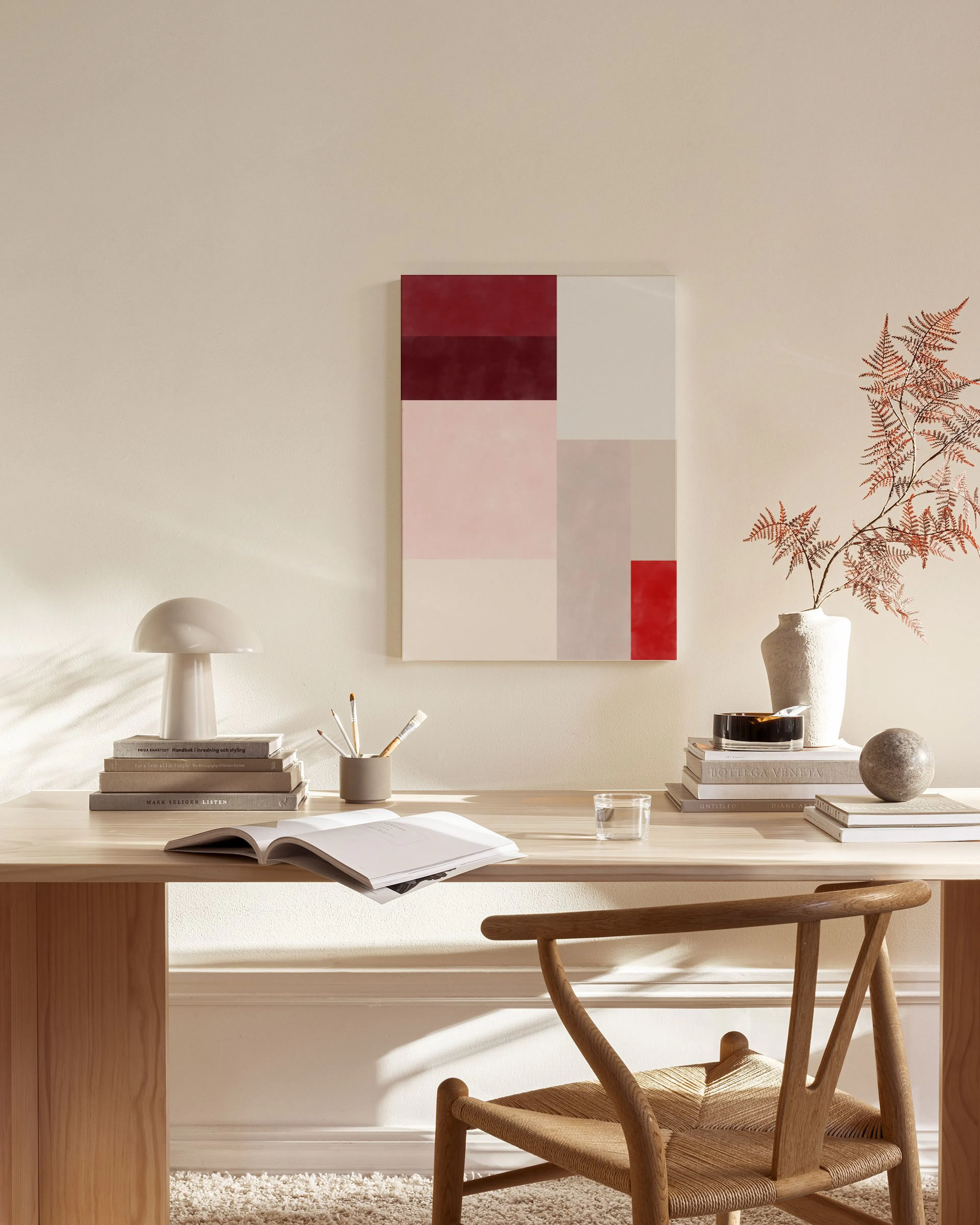 Lærred med geometrisk kunst i røde, rosa og grå nuancer, der hænger i en moderne stue over en træbænk.