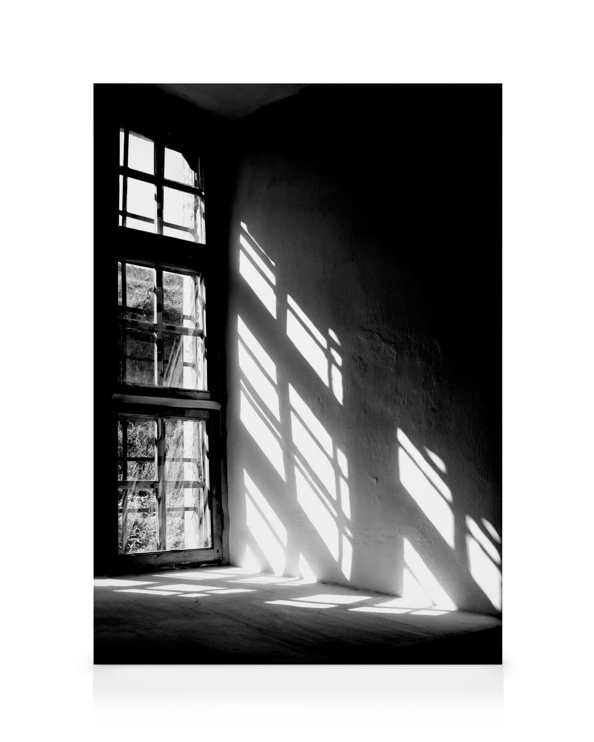 Schwarz-weiß-Foto eines Fensters mit Sonnenlicht, das durch die Scheiben fällt und Streifen auf die Wand und den Boden wirft.