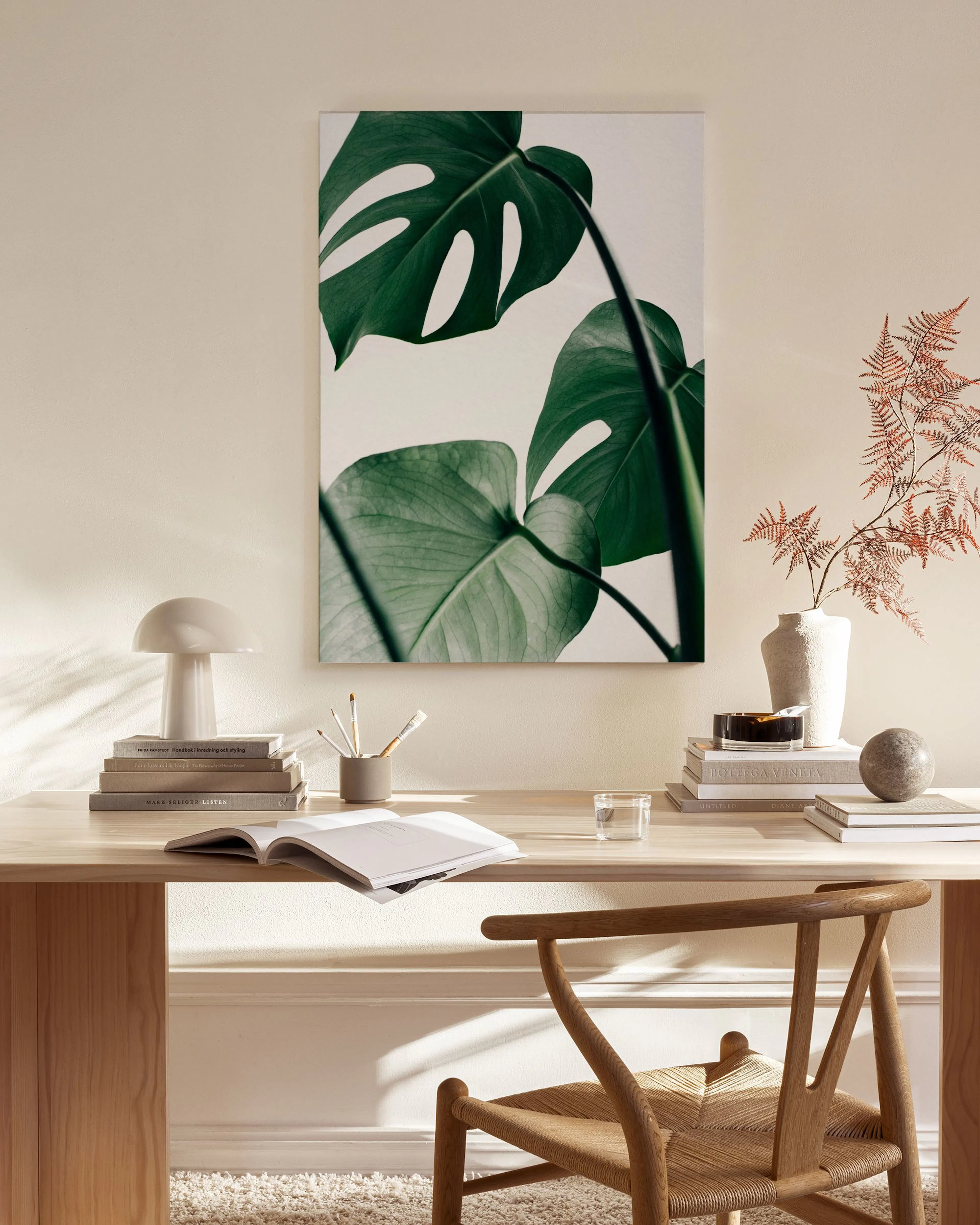 A canvas print of large green monstera leaves on a white background, hanging in a bright, minimalist living room.